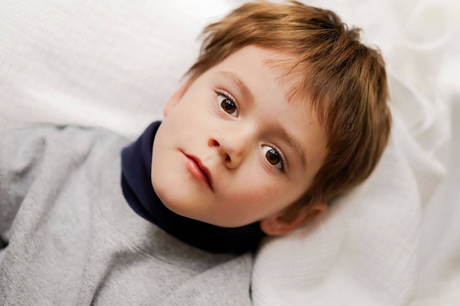 Child lying on white bedding looking up with curious expression.