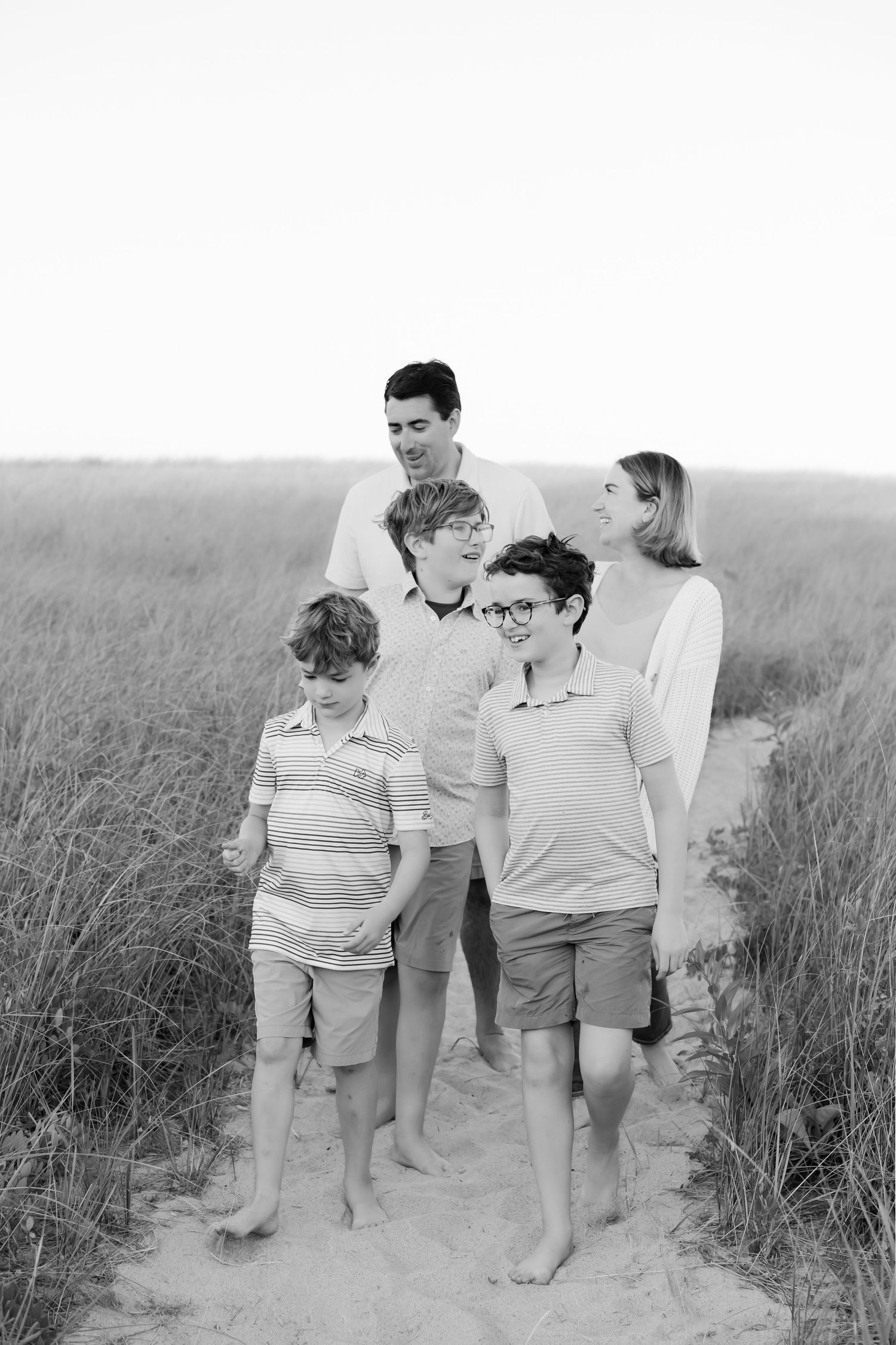 Black and white photo of a family standing together on a sandy path through beach grass.