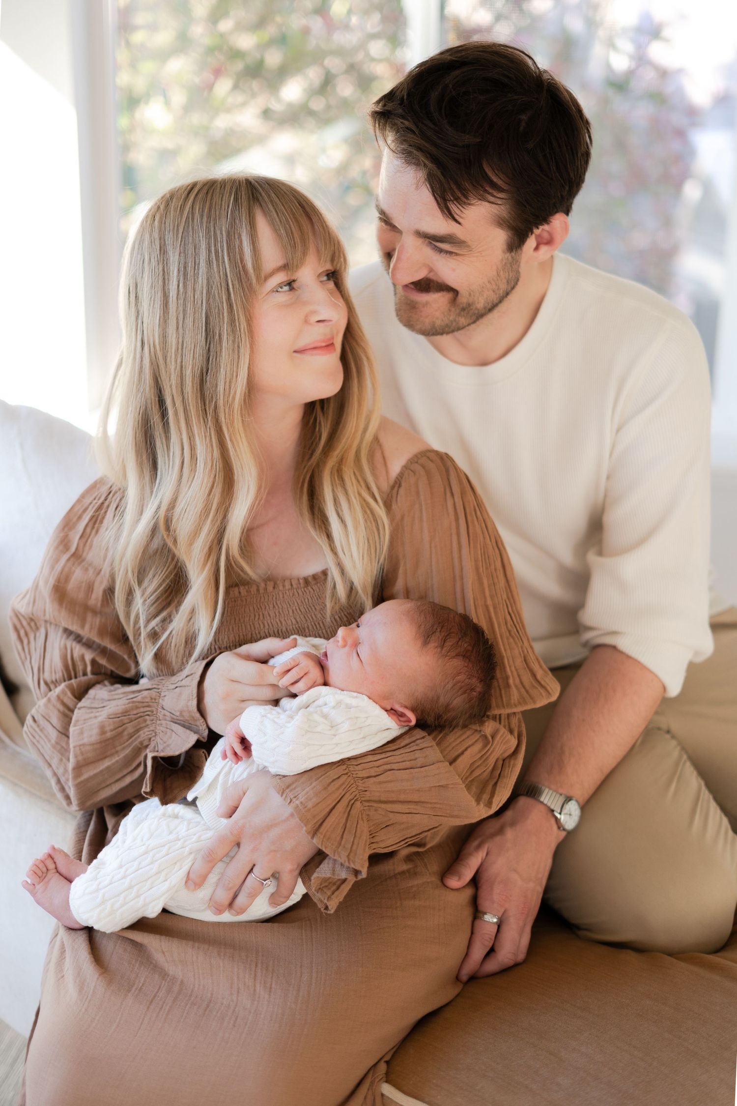 Intimate family portraits on a couch showing parents bonding with their newborn baby.