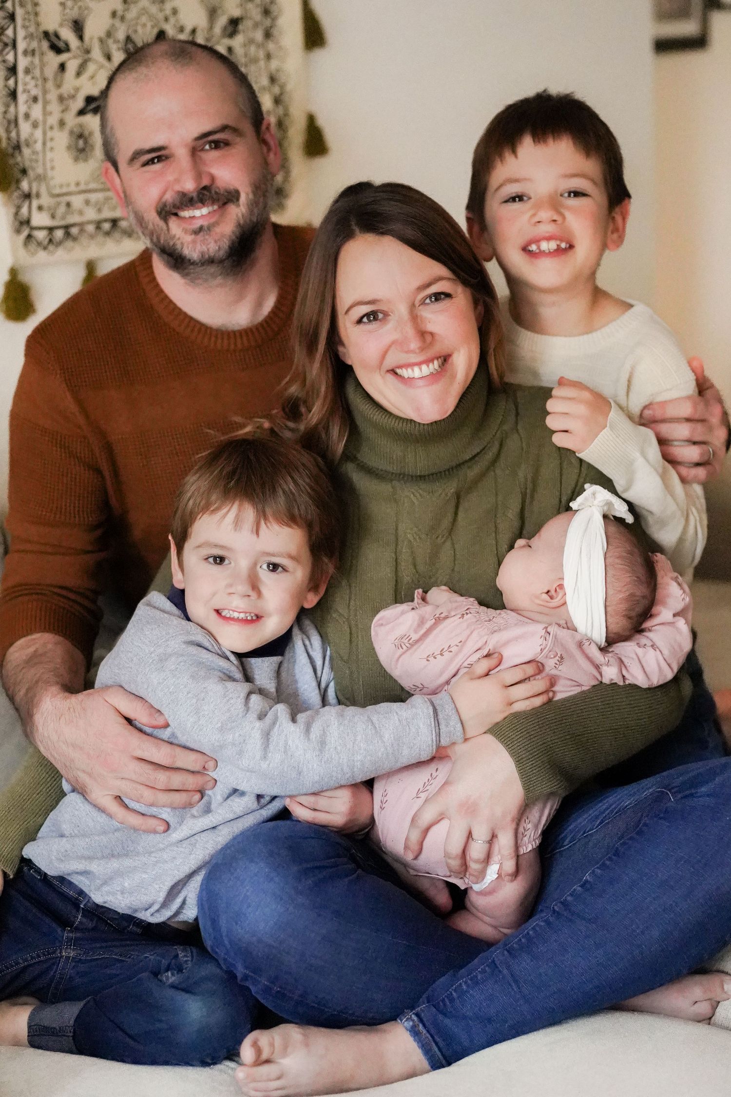 Indoor family portrait with coordinated earth tone outfits on grey couch.