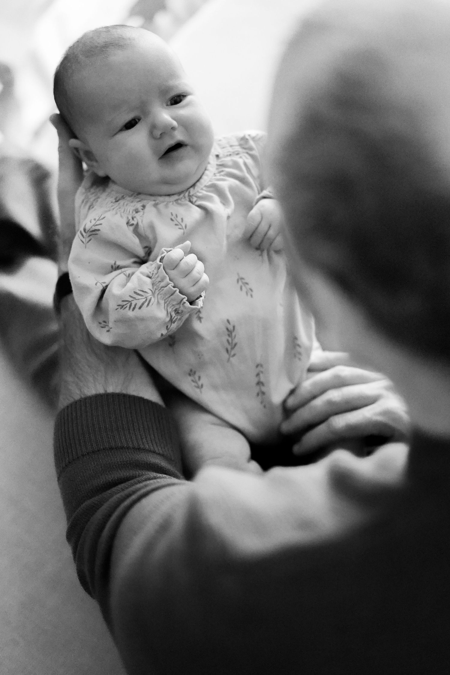 Black and white image of baby in floral outfit being held gently.