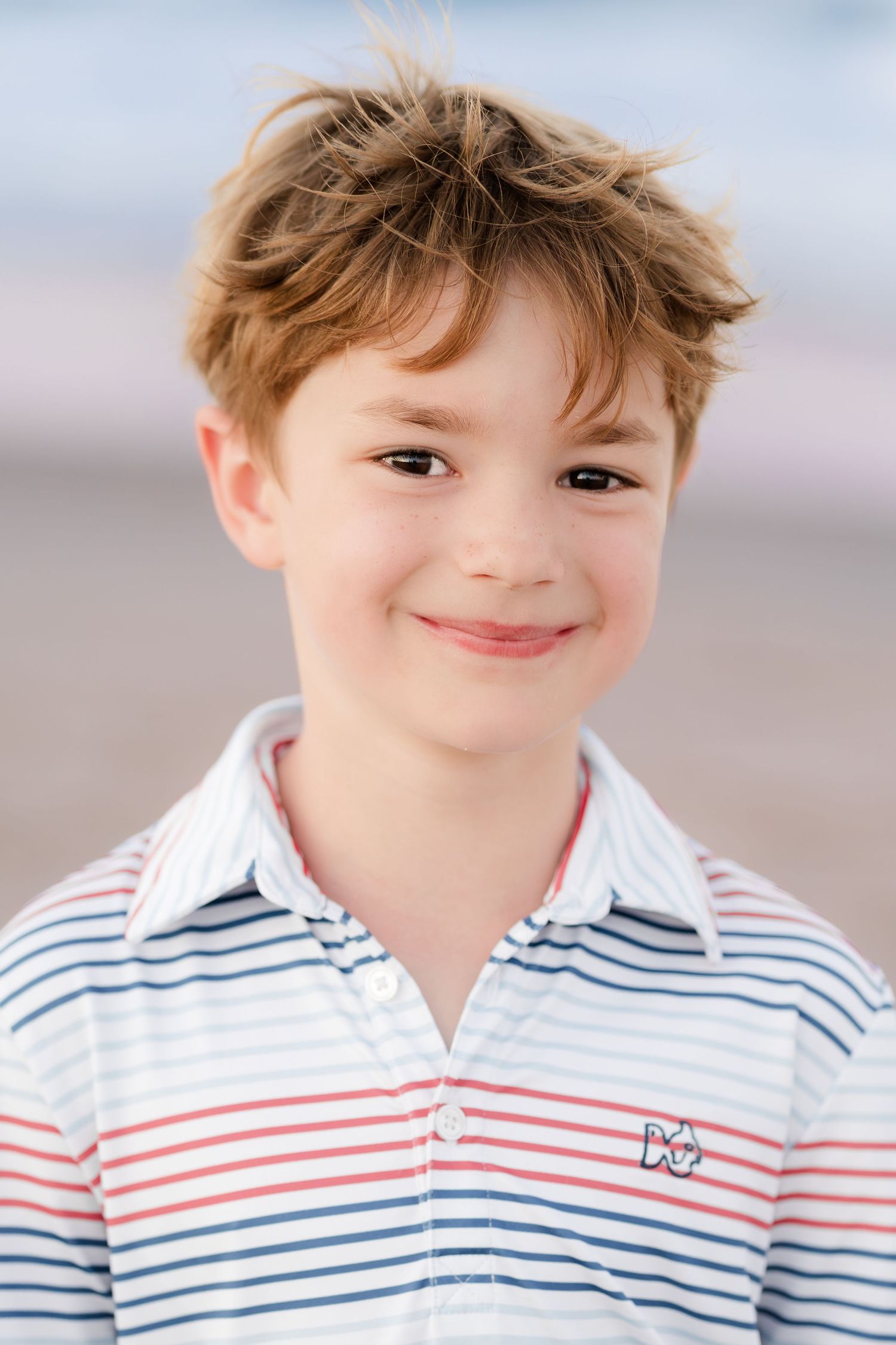 Close up portrait of a child in a nautical striped polo shirt at the beach.
