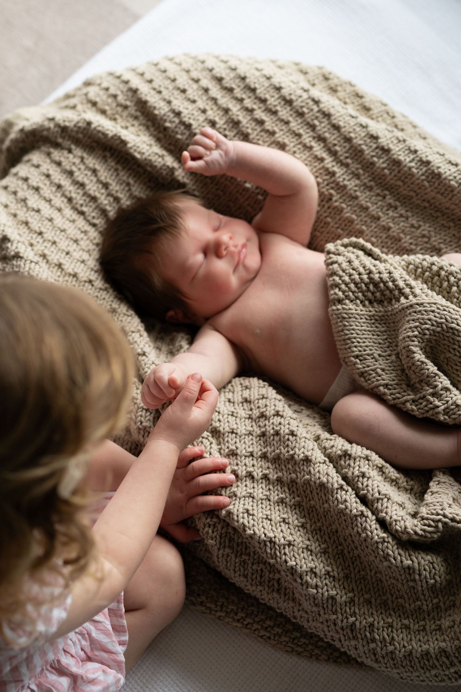 Infant sleeping peacefully on cozy knitted blanket in warm neutral tones.