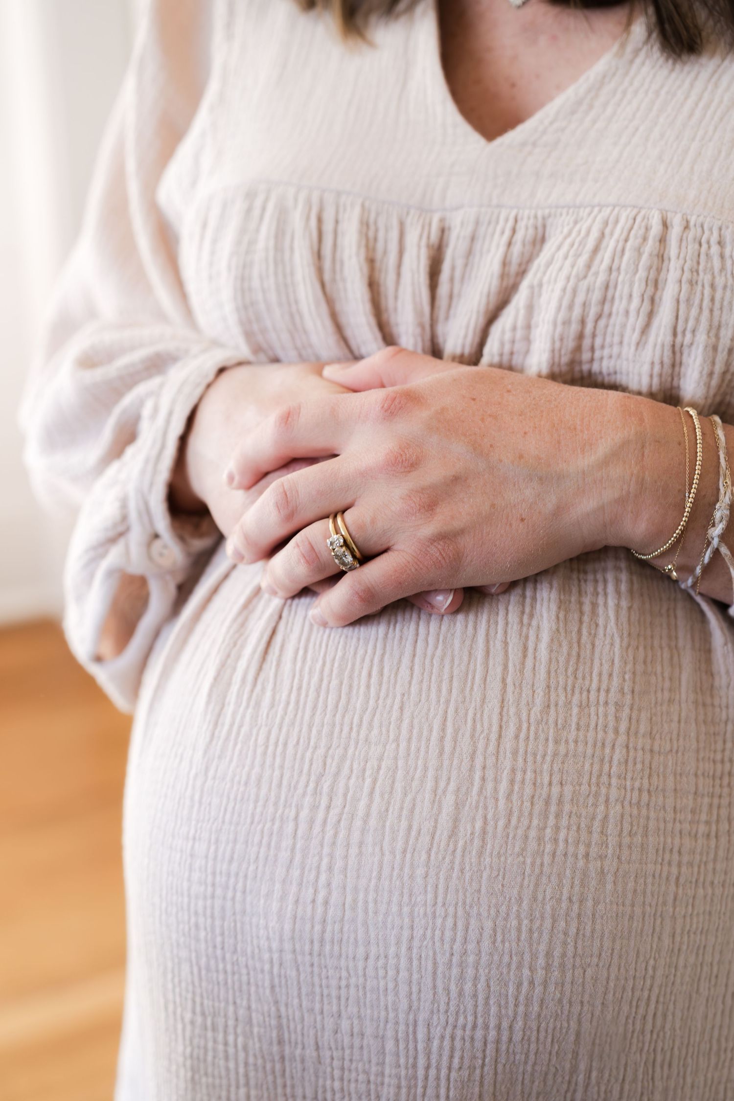 Close-up of hands gently resting on a pregnant belly in a white dress.