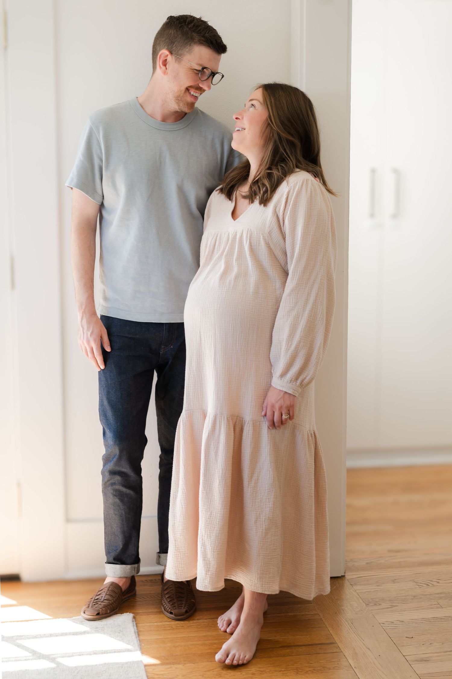 A couple stands together in a bright room with hardwood floors.