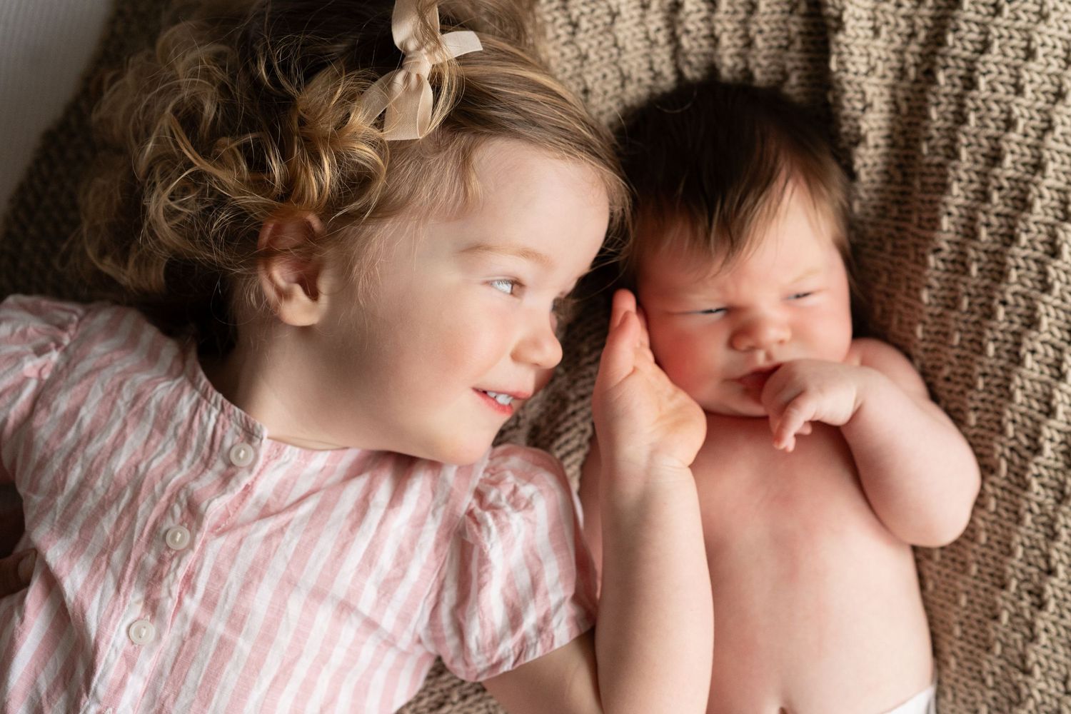 Two sleeping newborn babies lying together on soft blankets in matching outfits.