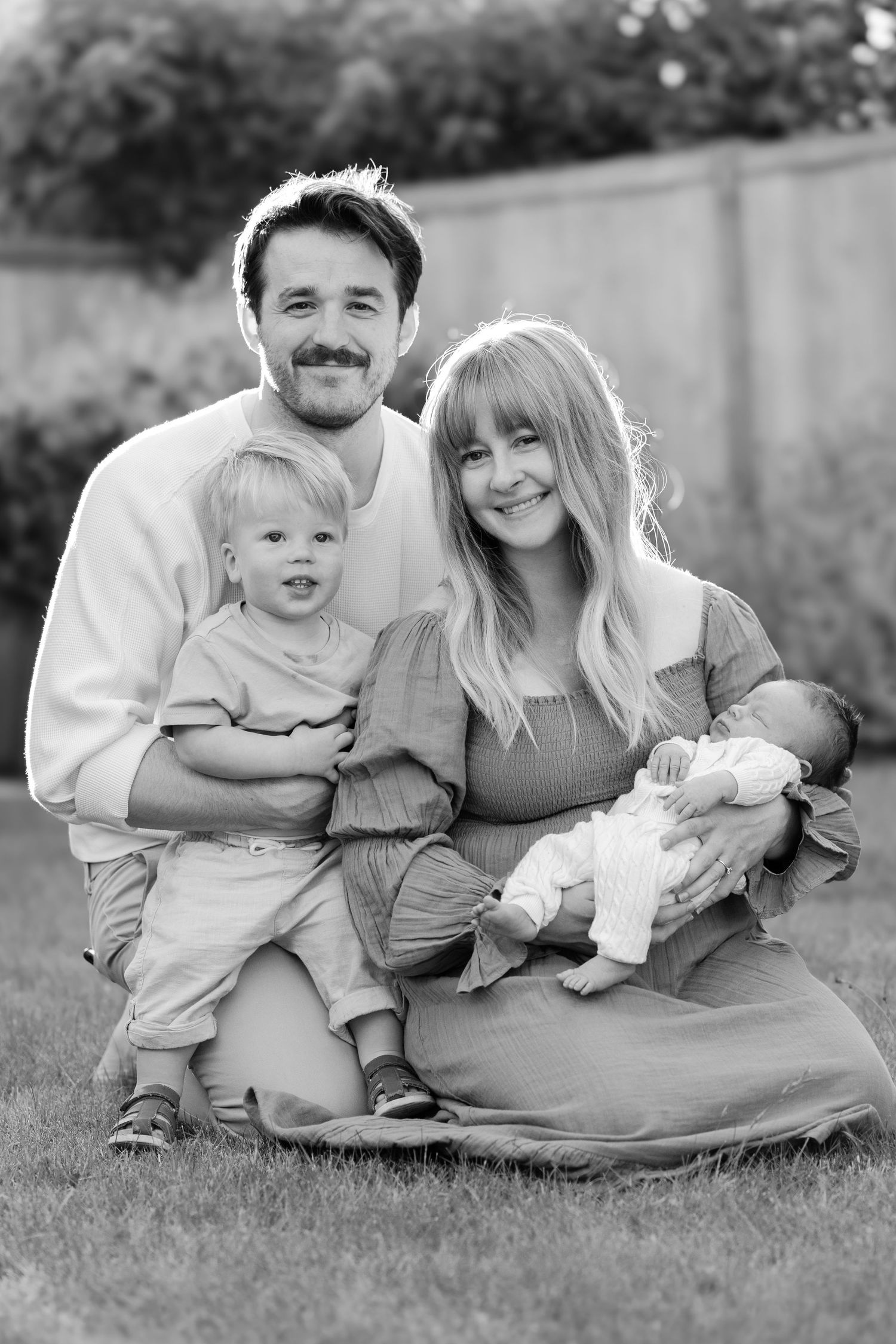 Black and white outdoor family photos showing parents with toddler and newborn on grass.