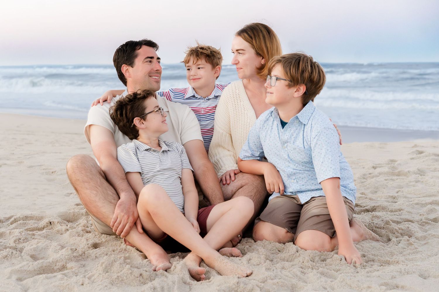 A family of five sitting close together on the beach during golden hour.