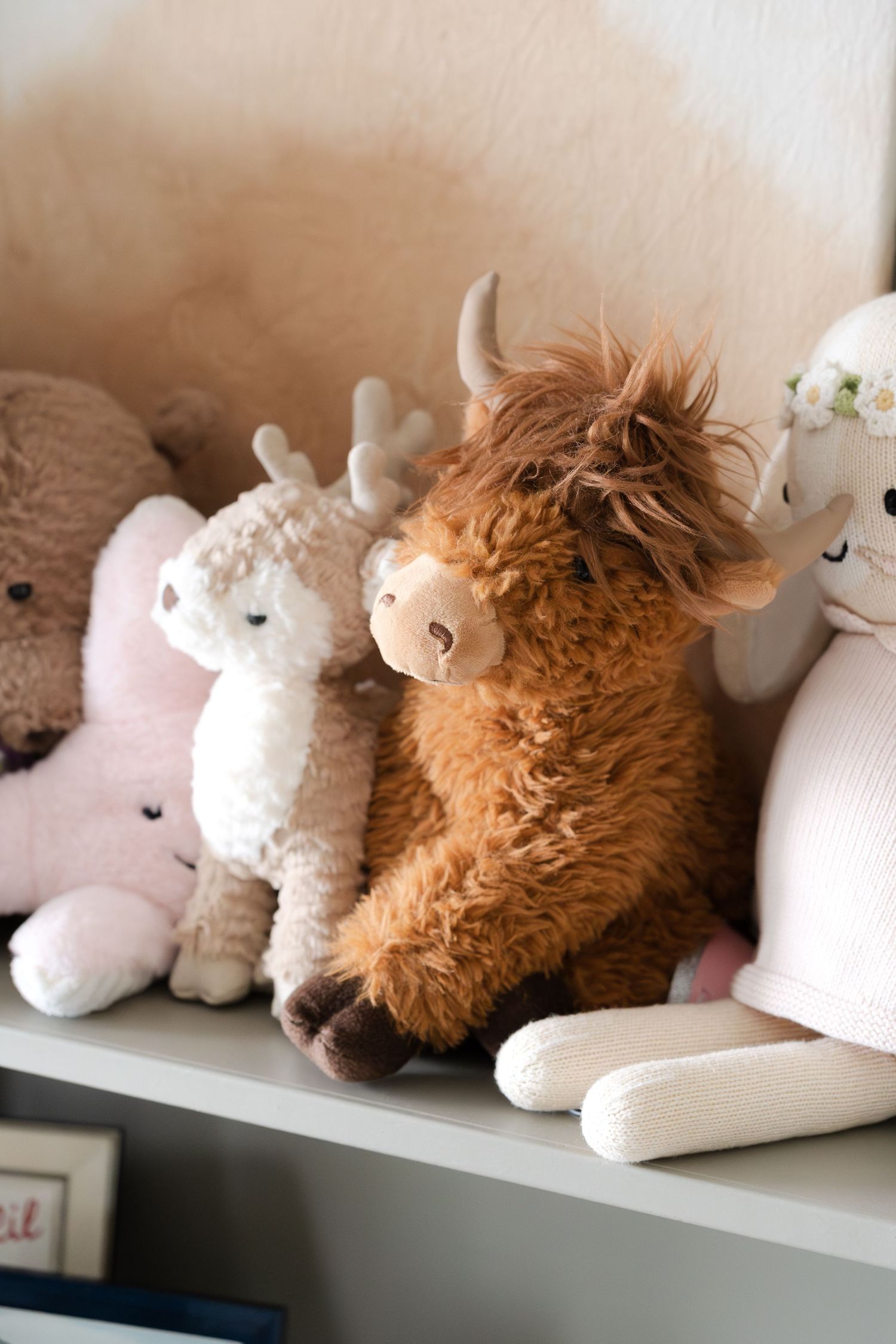 Plush stuffed animals including a highland cow and unicorns displayed on a nursery shelf.