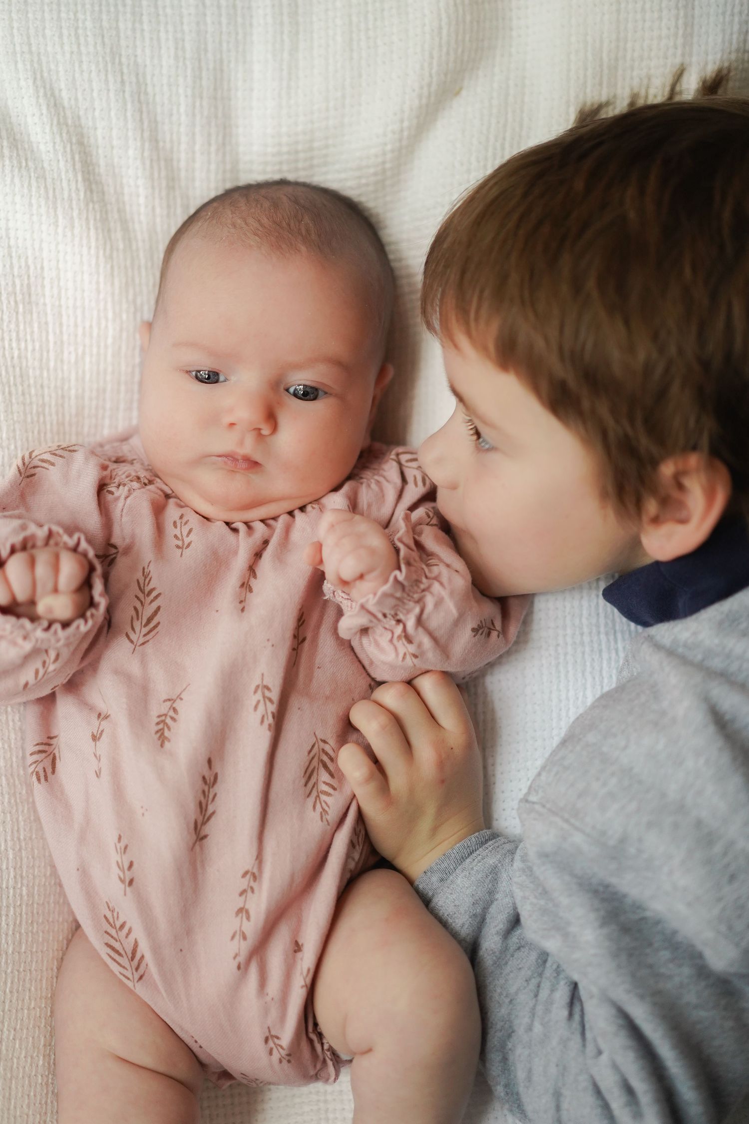 Sweet moment between siblings as older child leans in close to baby in pink romper.