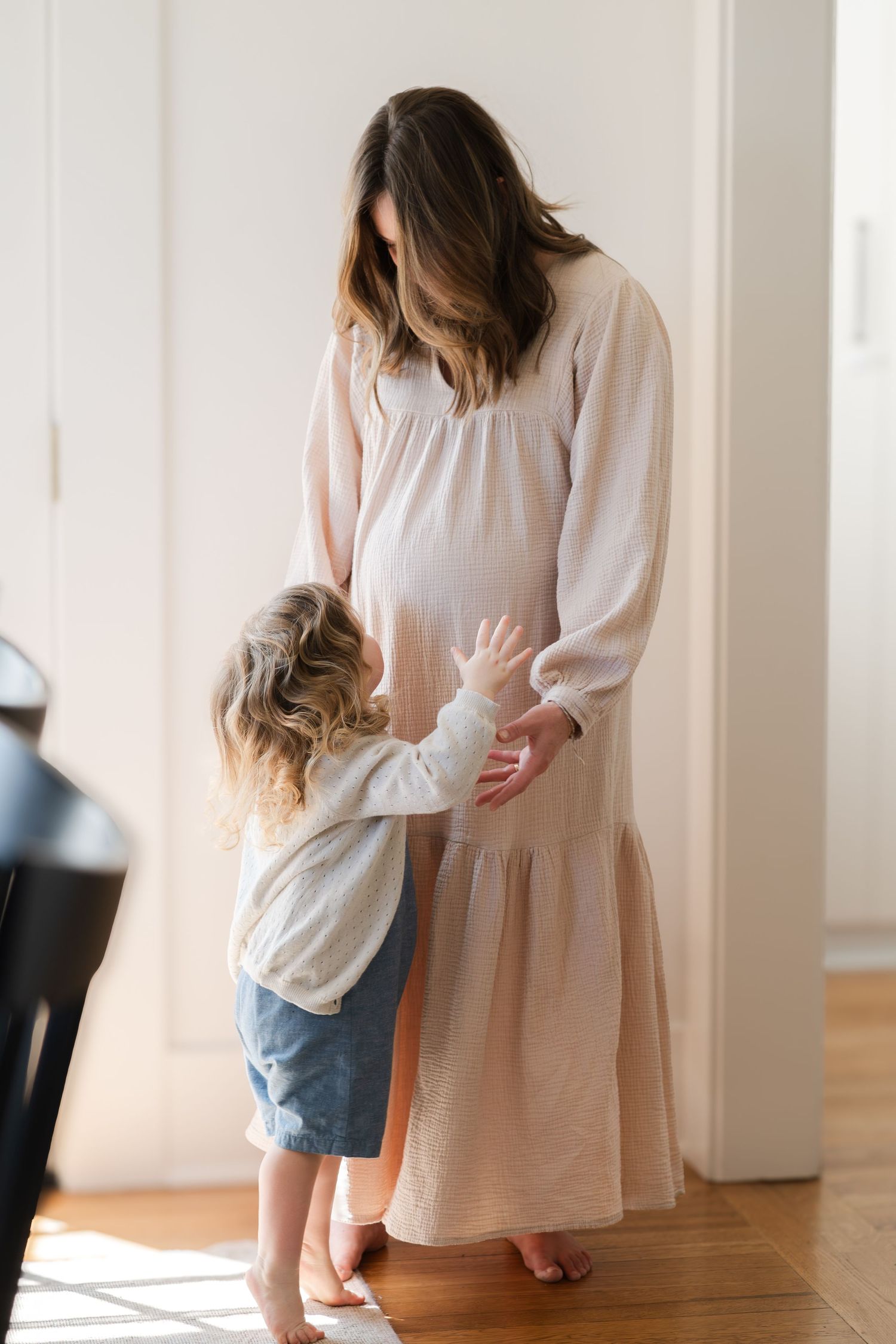 A tender moment between a parent in a cream dress and child in denim shorts.