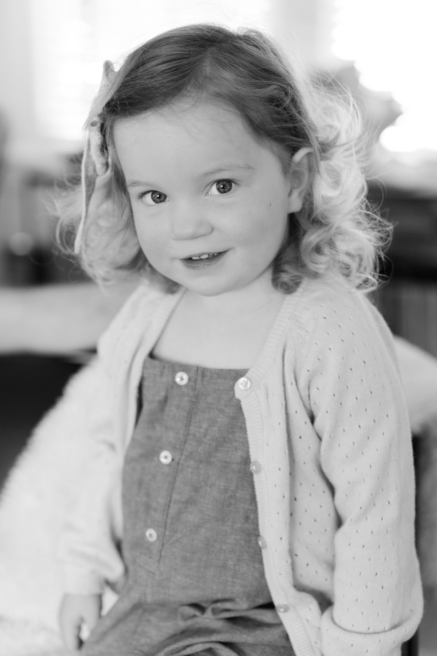 Black and white portrait of a young child in overalls with curly hair.