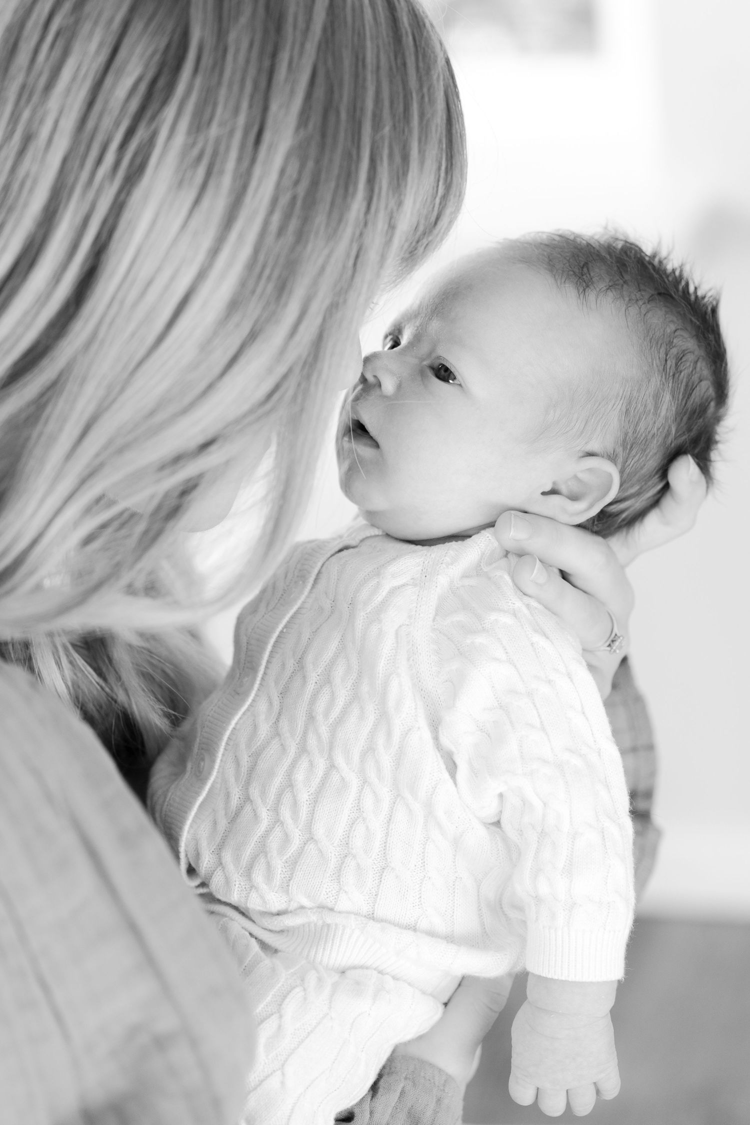 Intimate black and white portrait of parent holding baby in white knit outfit.