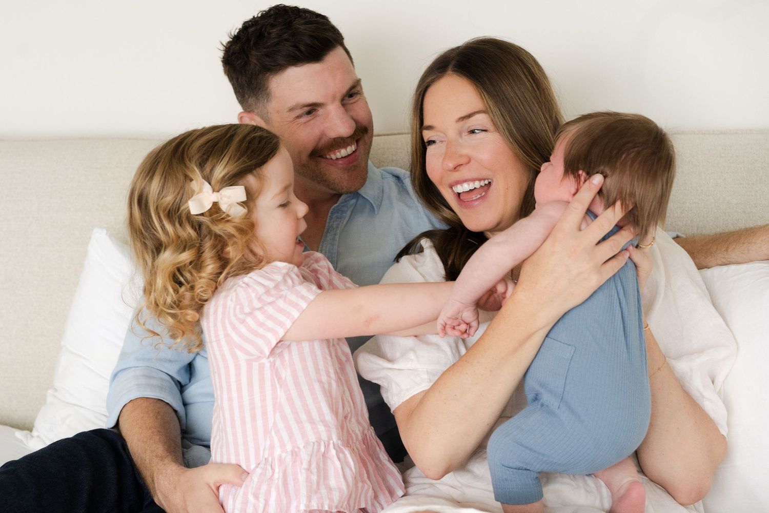 Happy family moment with everyone laughing and embracing on bed.