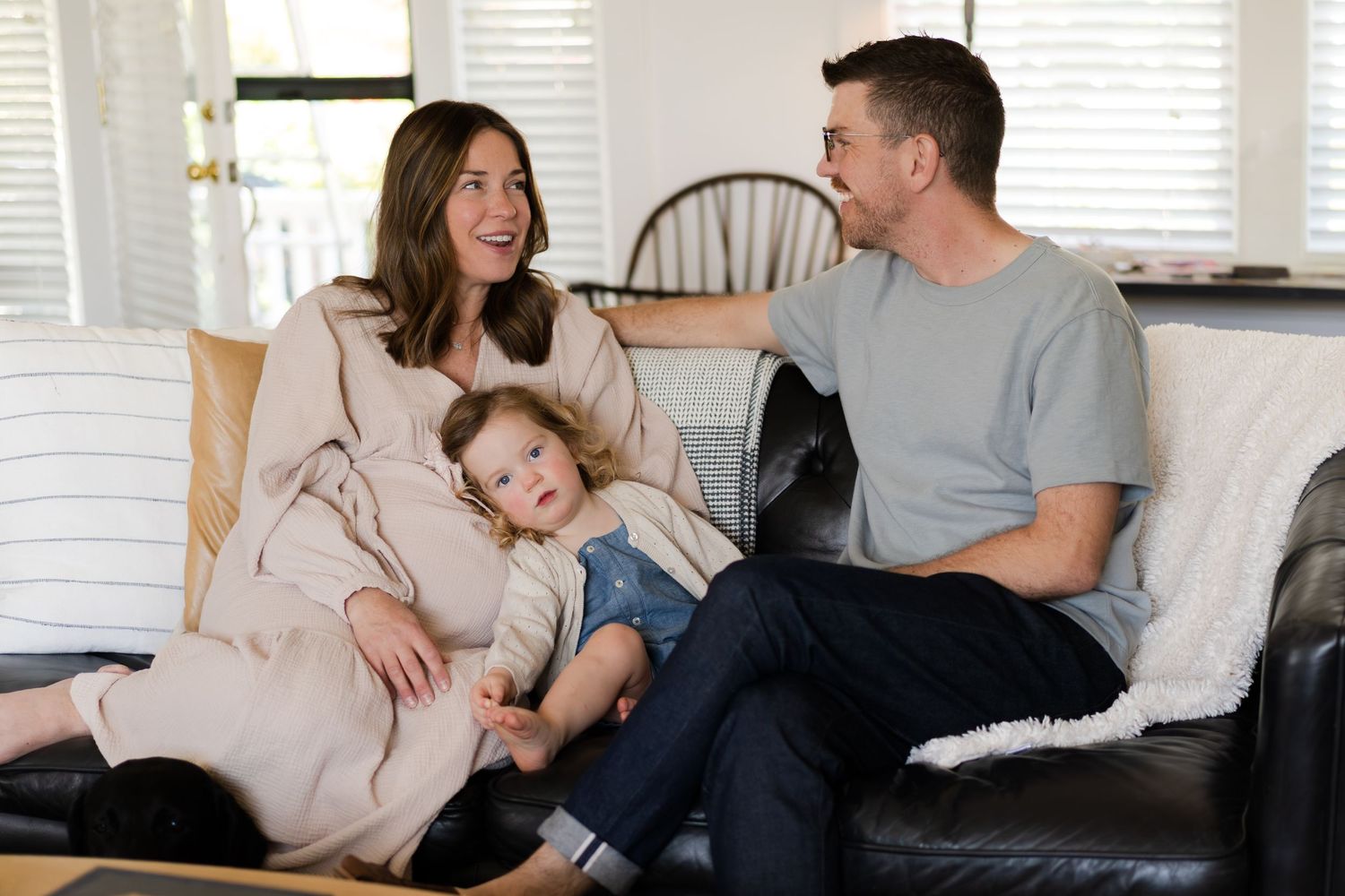 Family lounging together on white couch in bright room.