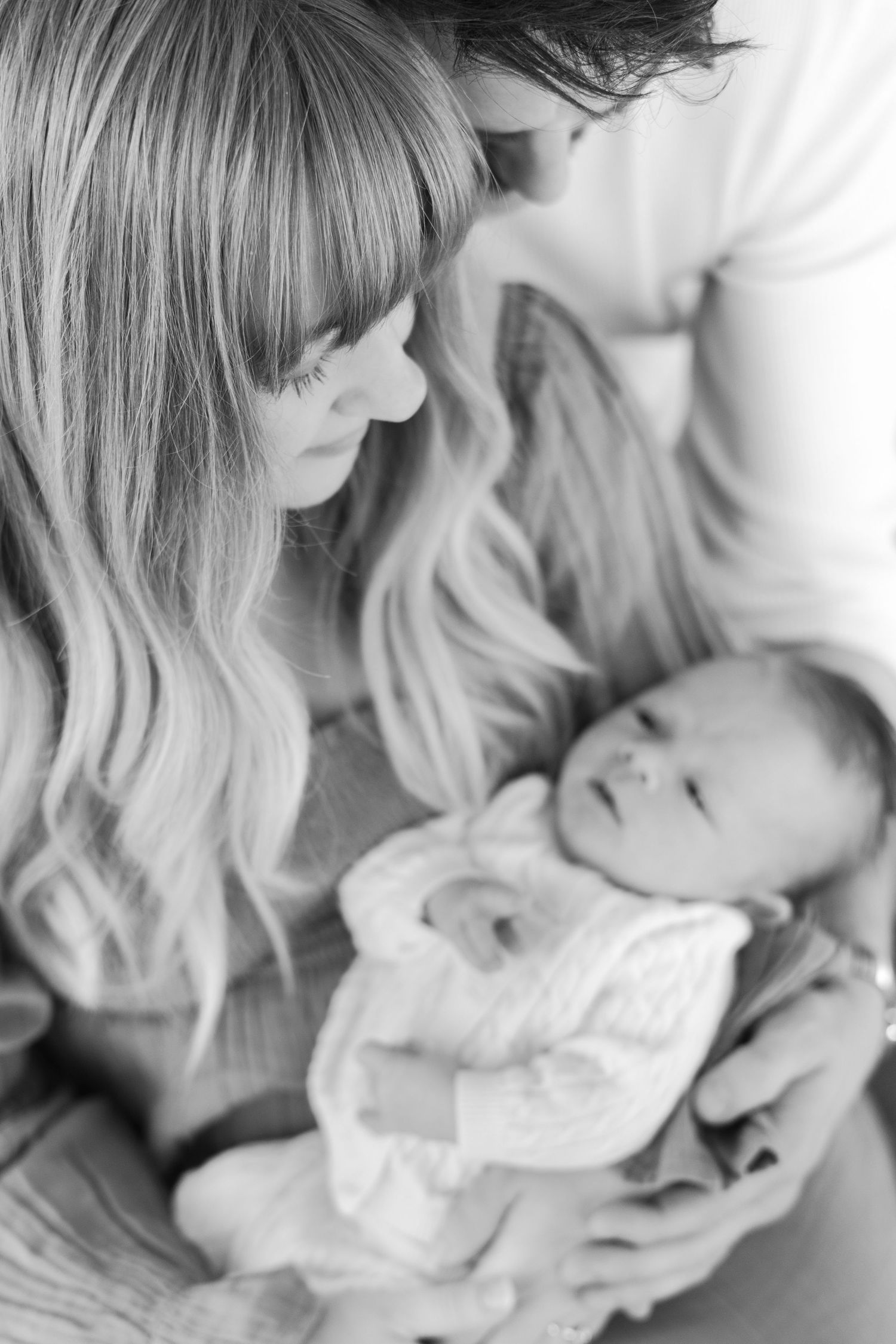 Tender black and white moment between parent and newborn in soft lighting.