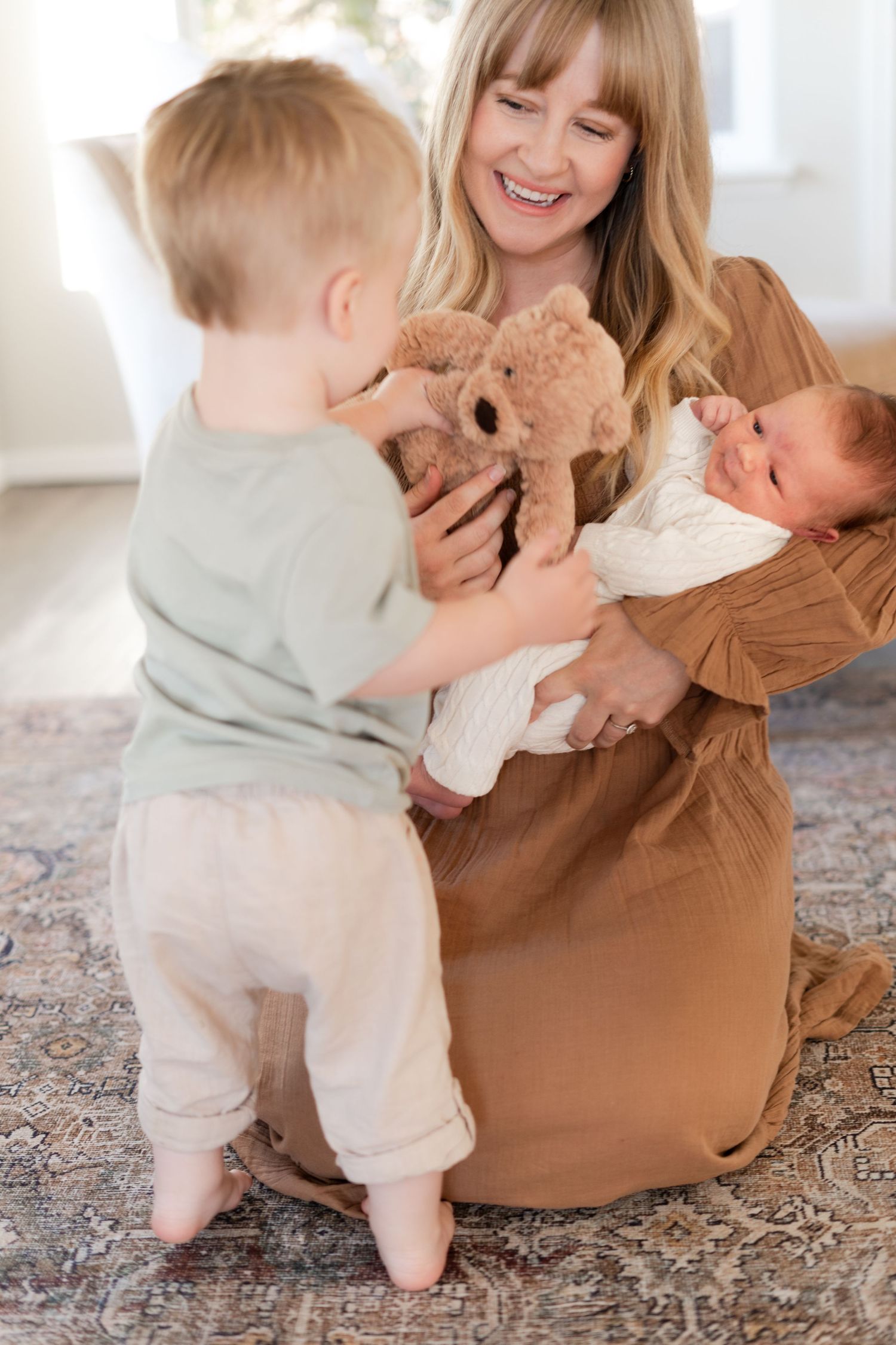 Family moment with teddy bear and baby on patterned rug.
