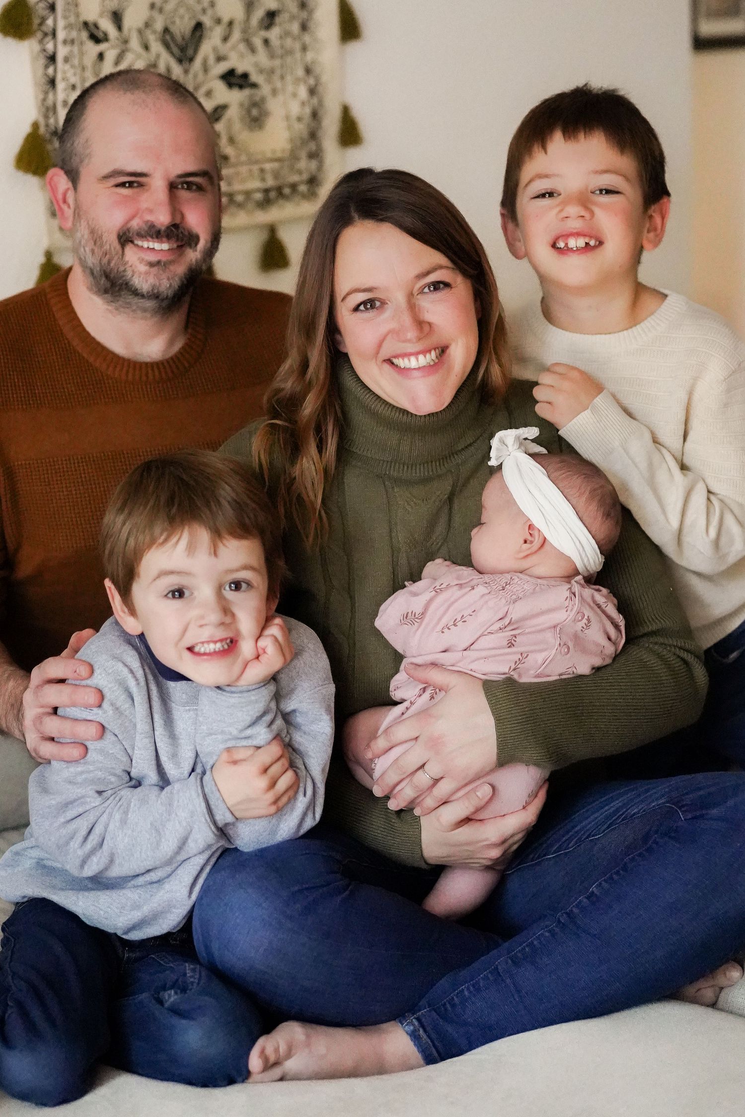 Indoor family portrait of five people sitting together on a couch with decorative wall hanging.