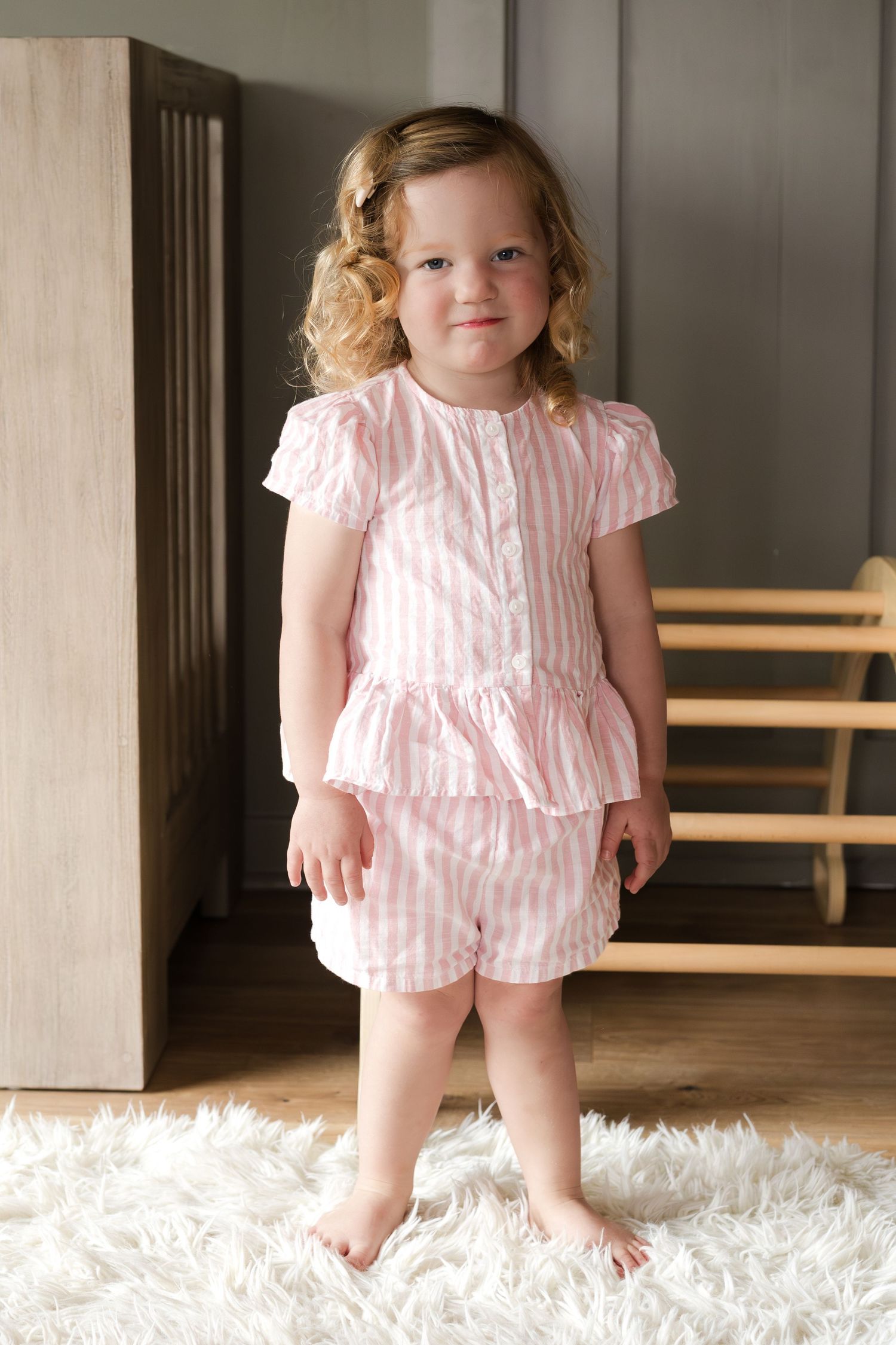 A charming pose in a pink striped outfit standing on a white rug.