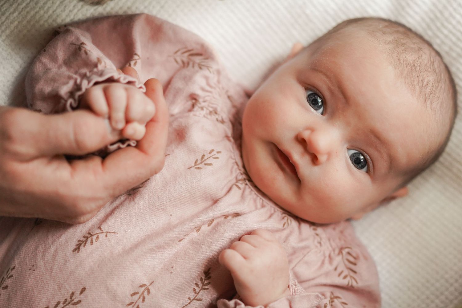 Close-up of baby in floral romper with hands gently touching fabric.