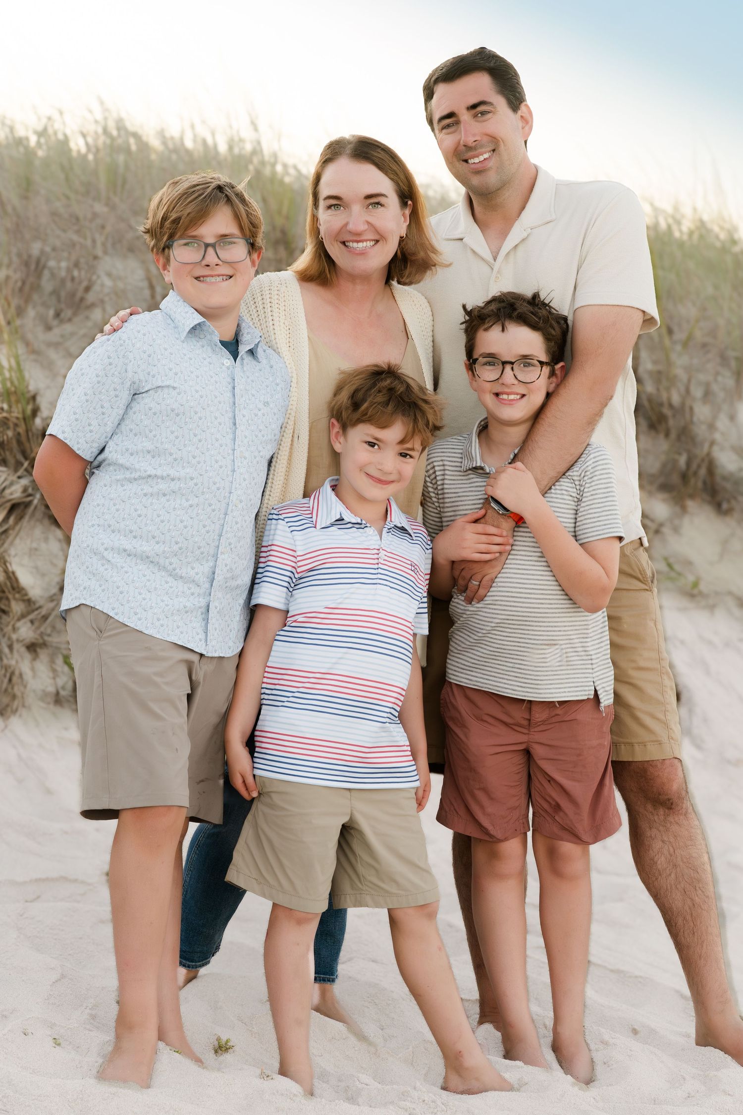 Family of four posing together on sandy beach dunes during a summer photoshoot.