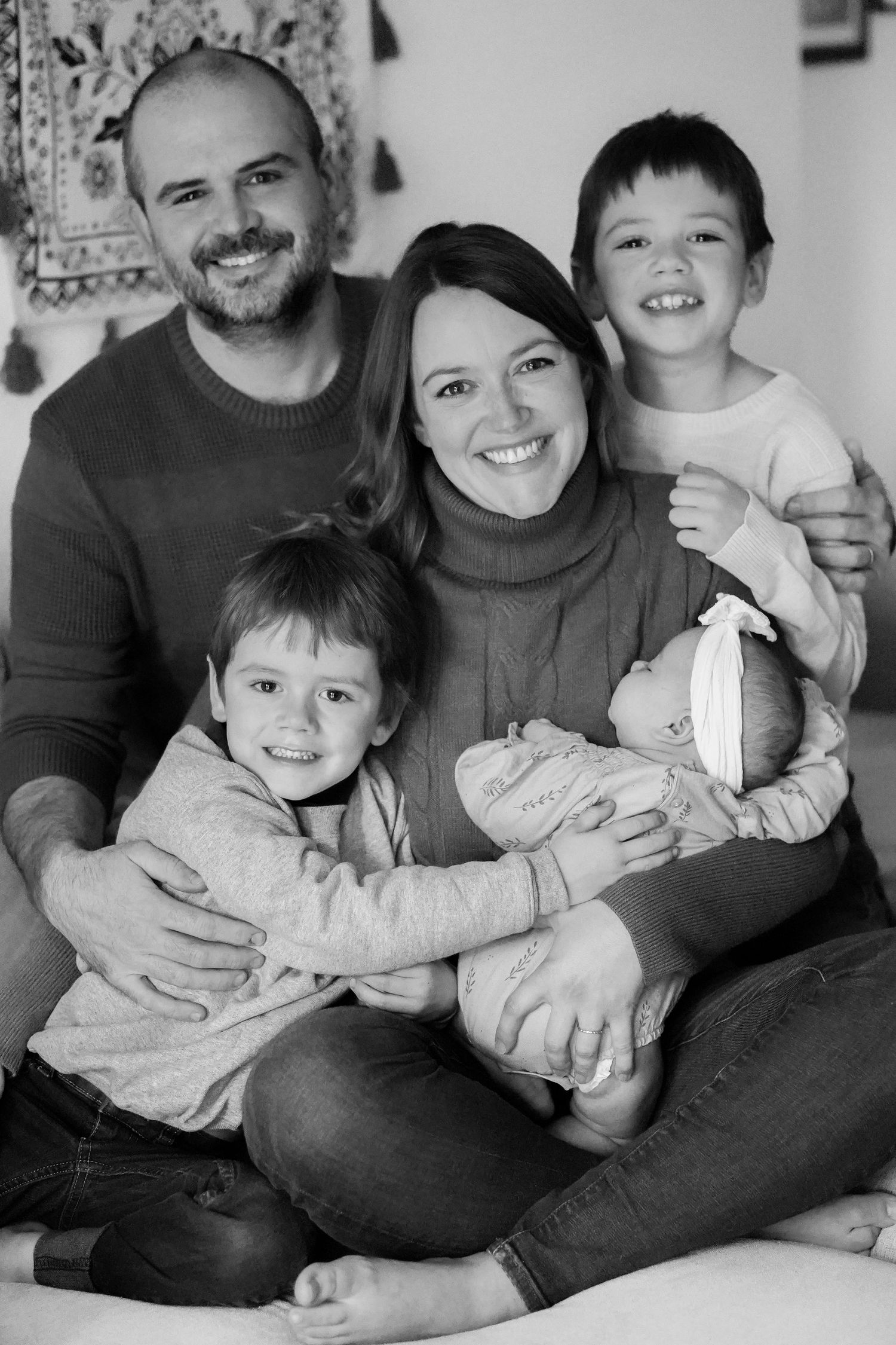 Black and white family portrait with decorative wall tapestry in background.