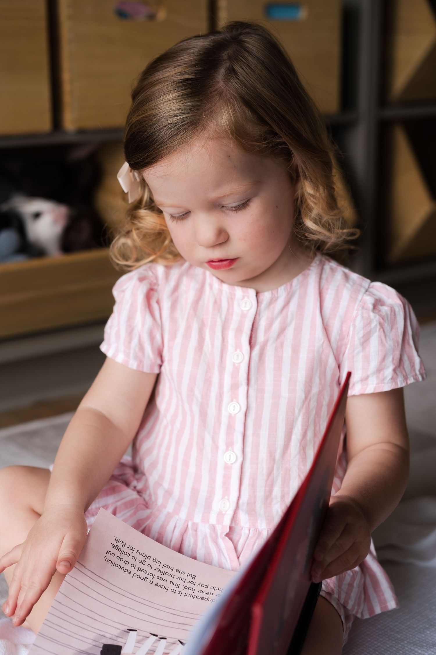 Young child in pink striped dress reading a book intently.
