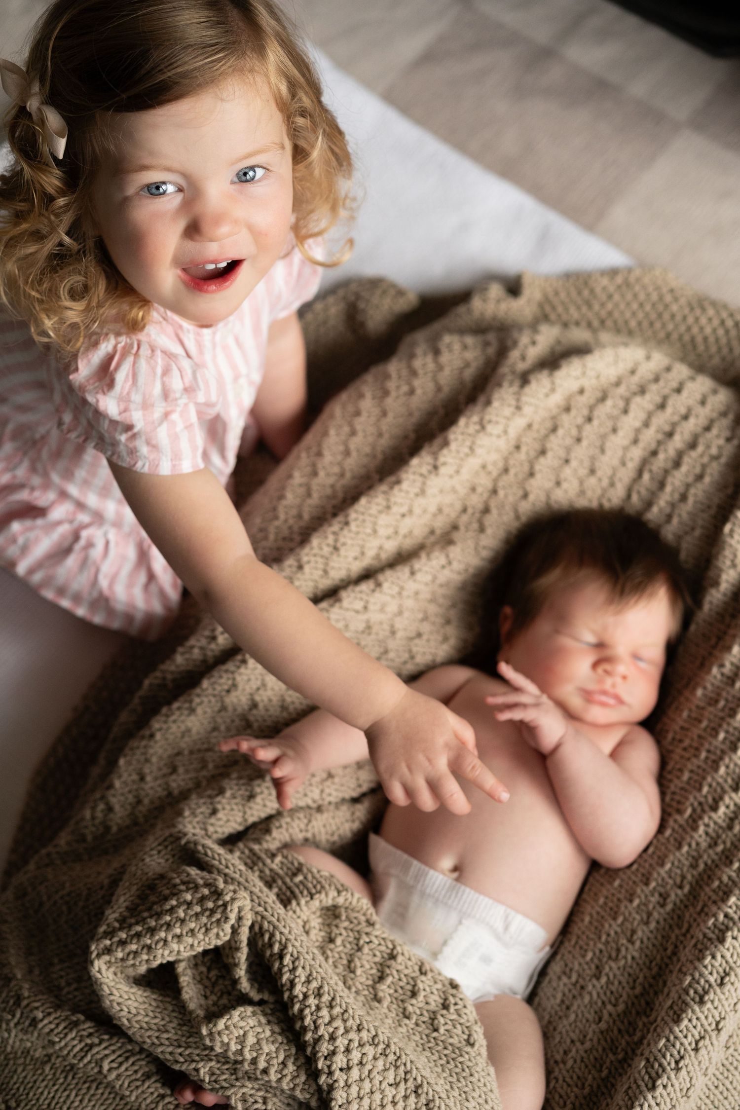 Two small children sharing tender moment on knitted blanket during photo session.