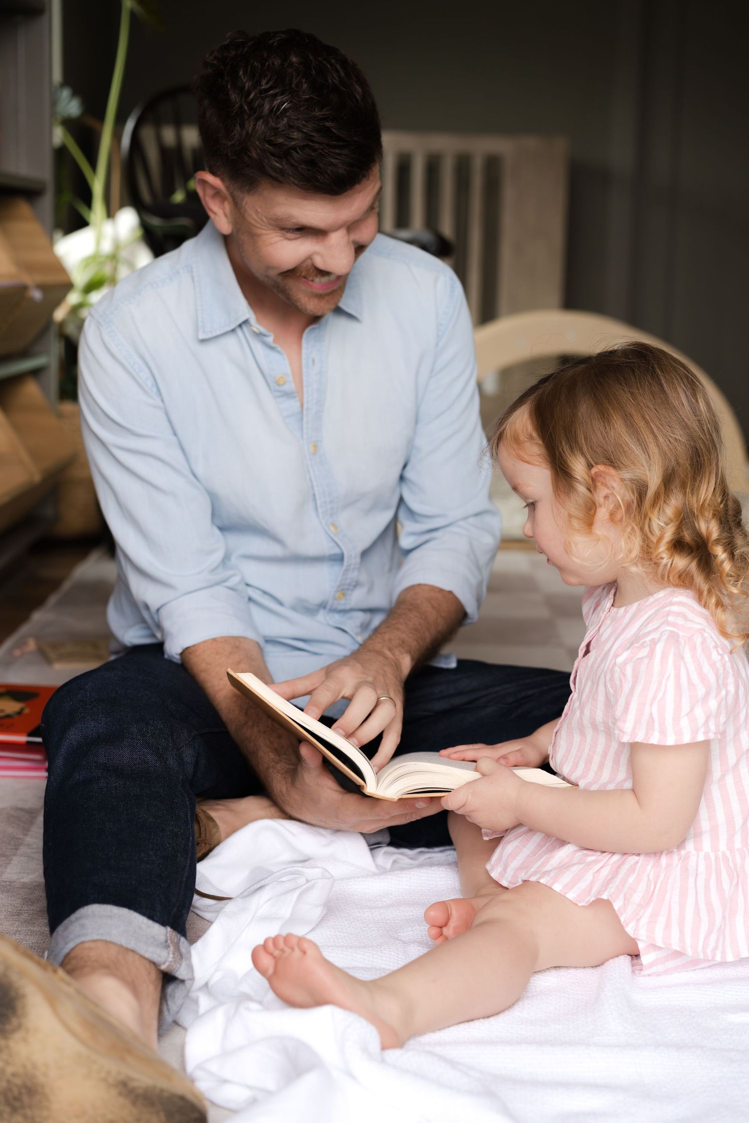 Parent and child sharing a quiet moment reading together on white bedding.