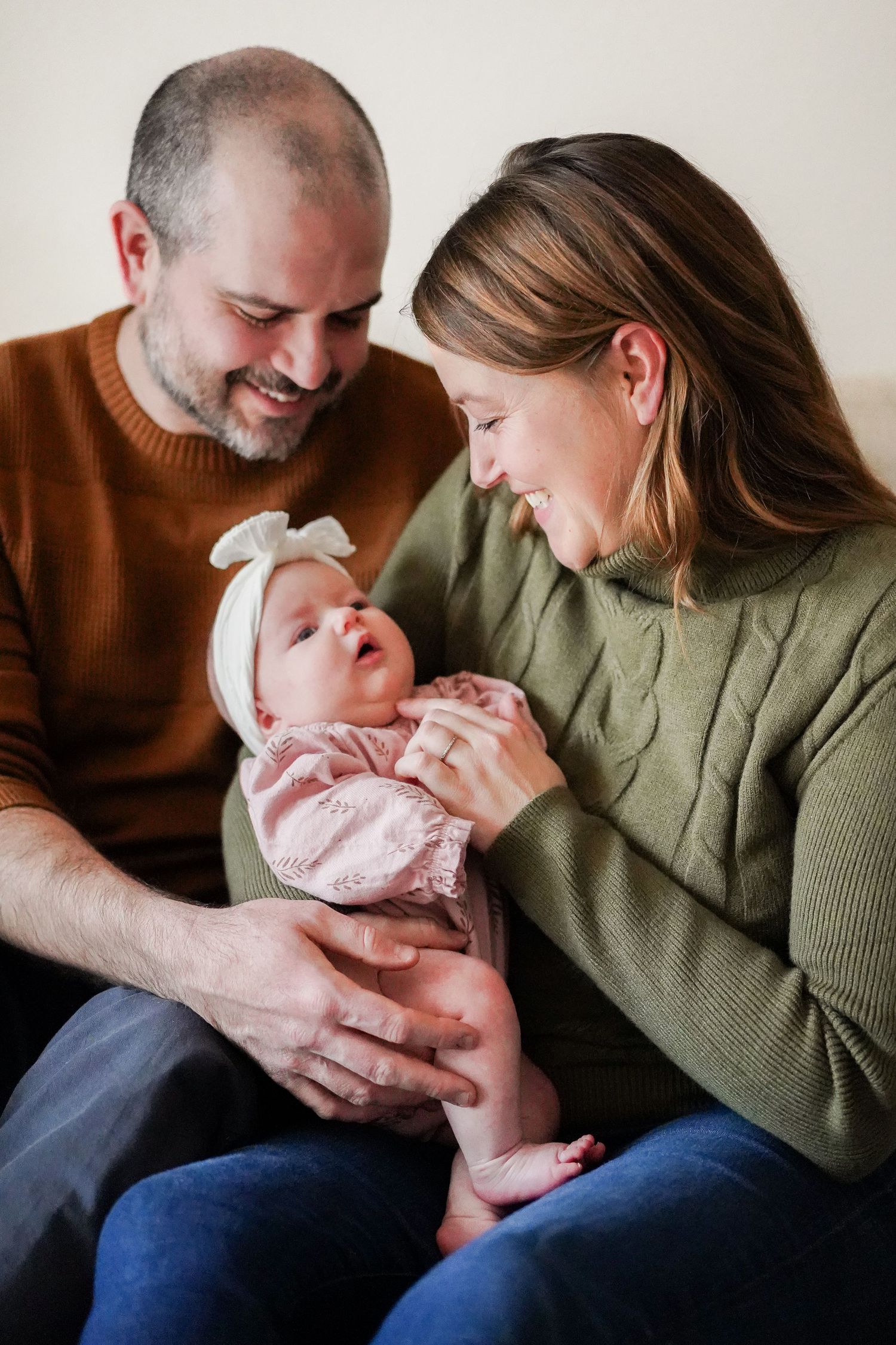 Parents in casual sweaters sharing joyful moment with infant in pink outfit.