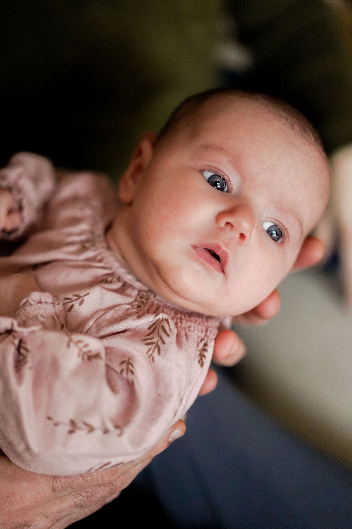 Close-up portrait of infant in pink floral outfit showing bright blue eyes and soft expression.