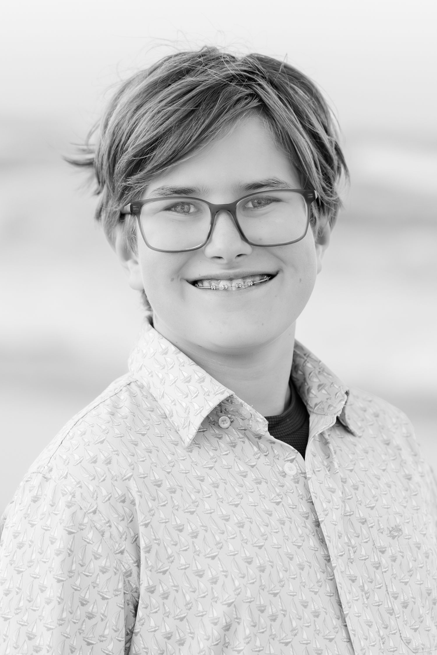 Black and white portrait of a young person wearing glasses and a patterned shirt.
