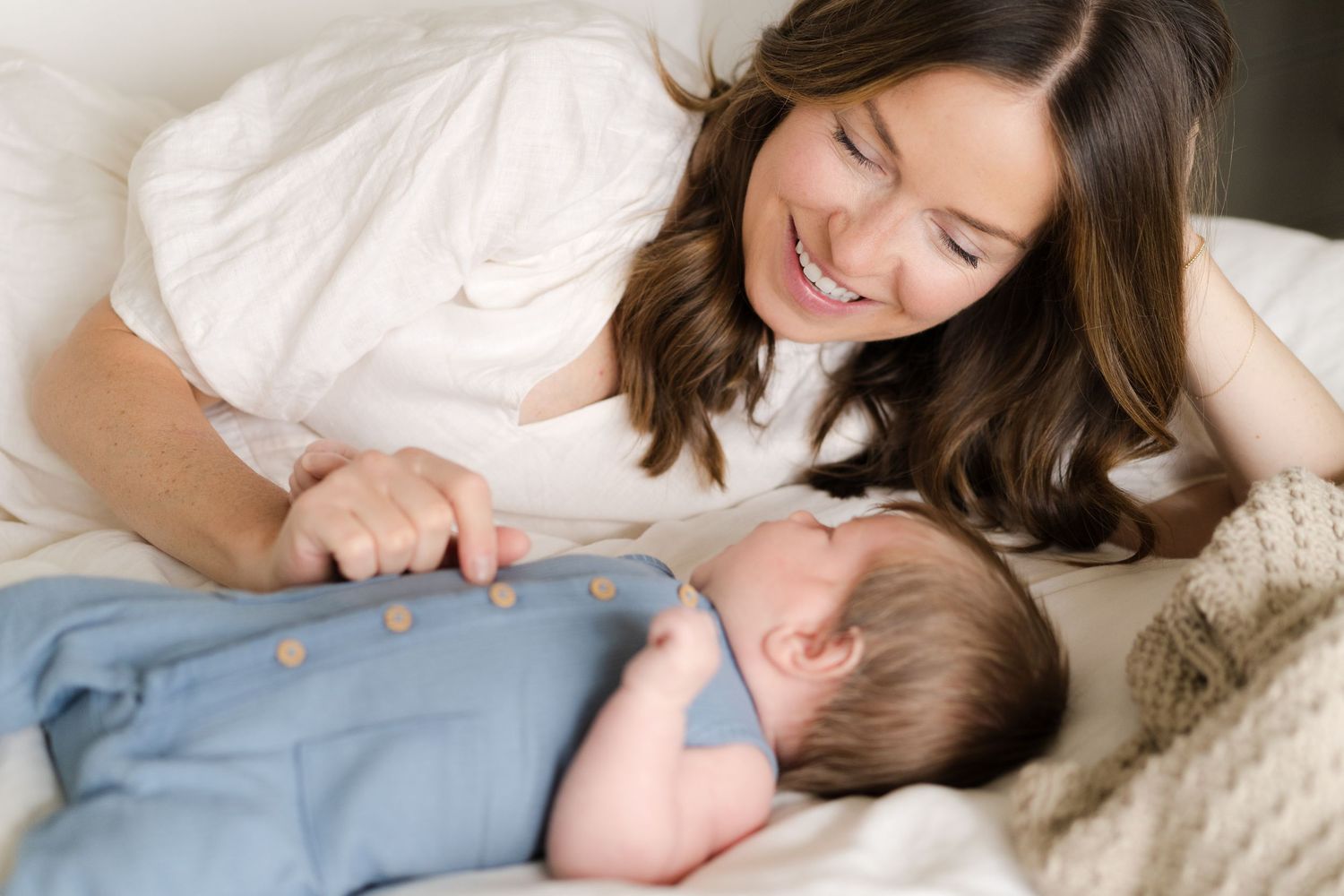 A tender moment between parent and baby lying together on white bedding.