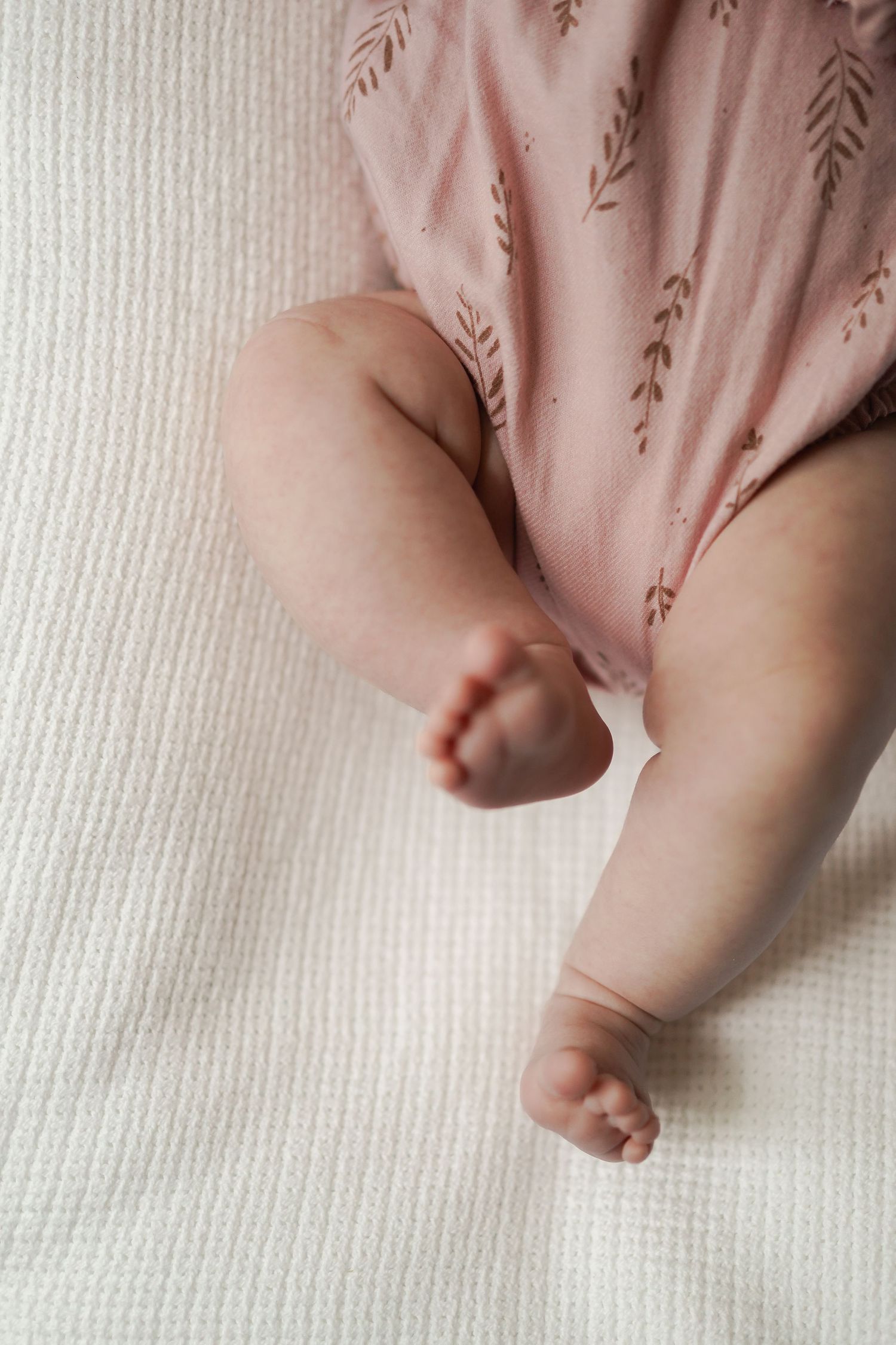 Close-up of tiny baby feet and legs against pink patterned fabric on white background.