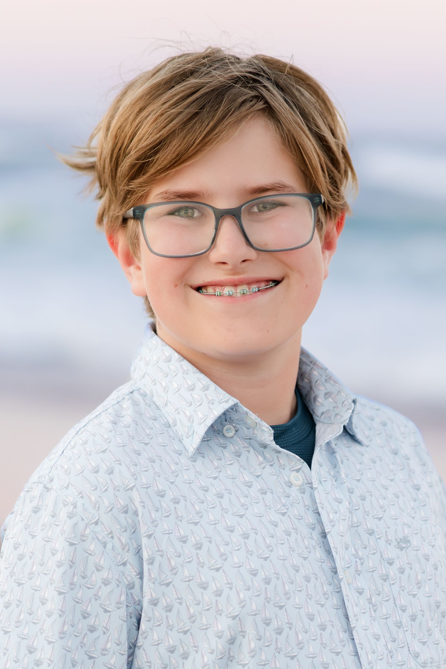 Young person in floral print shirt and glasses smiling at beach.