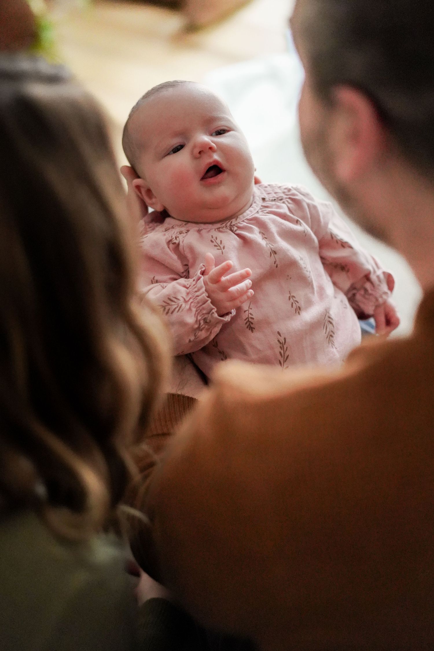 Baby wearing pink floral outfit smiling during intimate family moment.