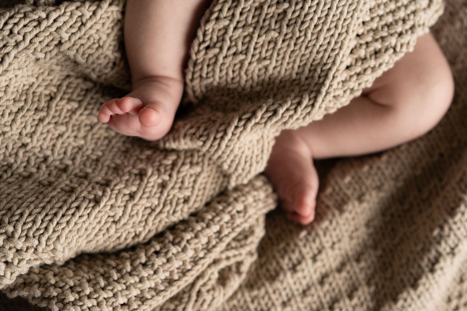 Close-up detail of tiny baby feet against soft knitted beige blanket texture.