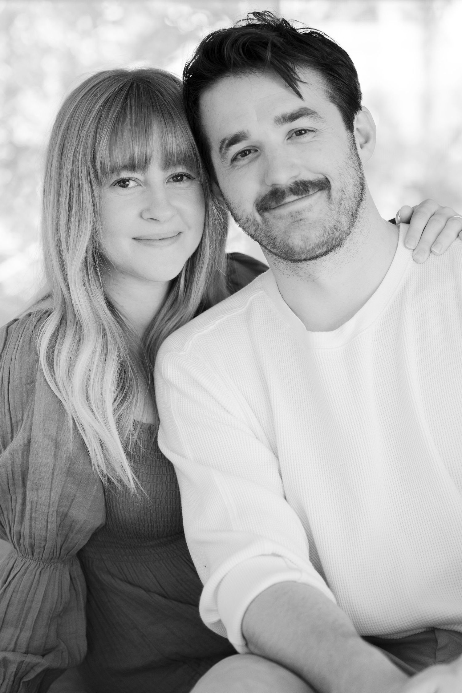 Black and white portrait of a couple smiling together in casual attire.