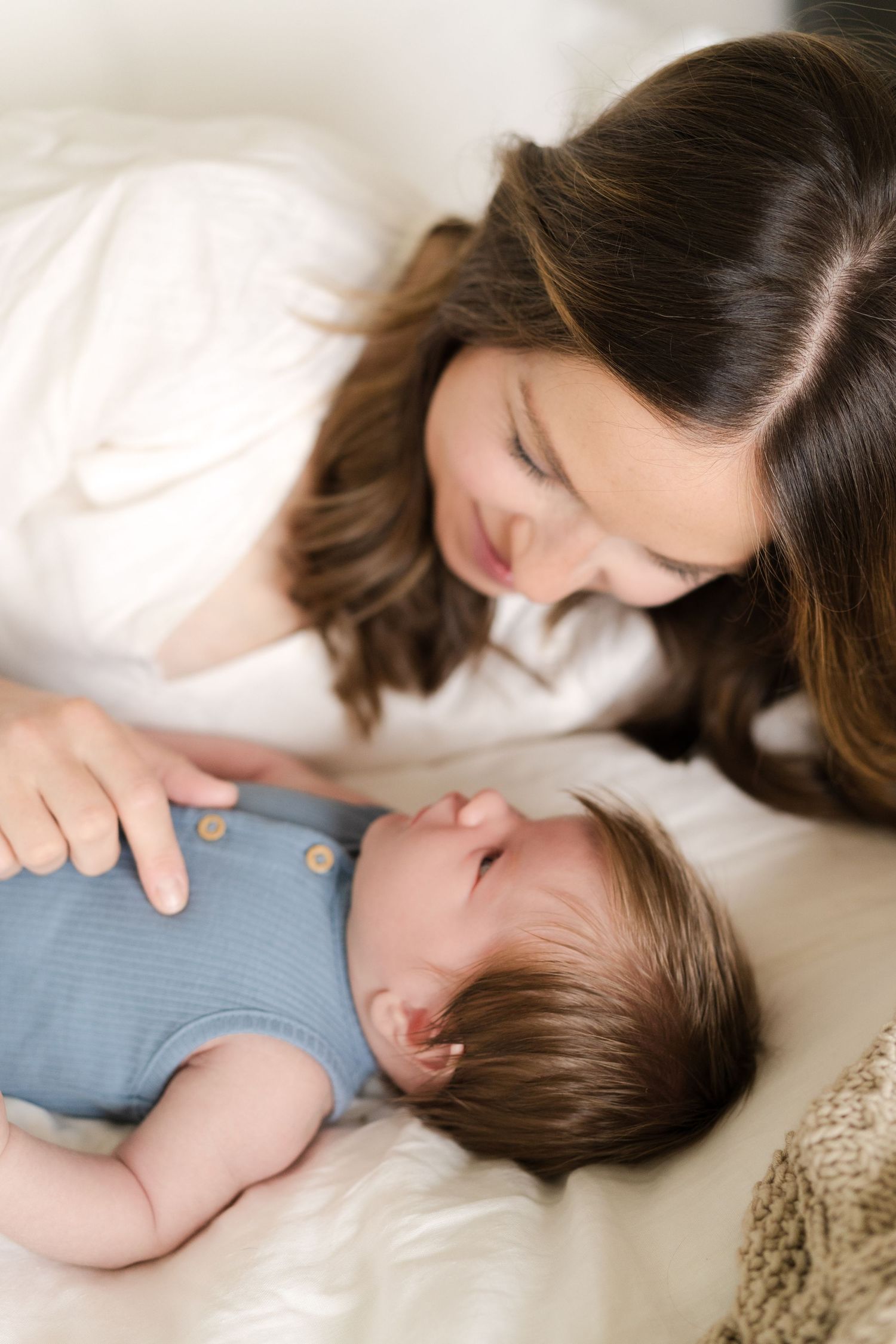 Close-up of parent snuggling with infant on soft white blankets.