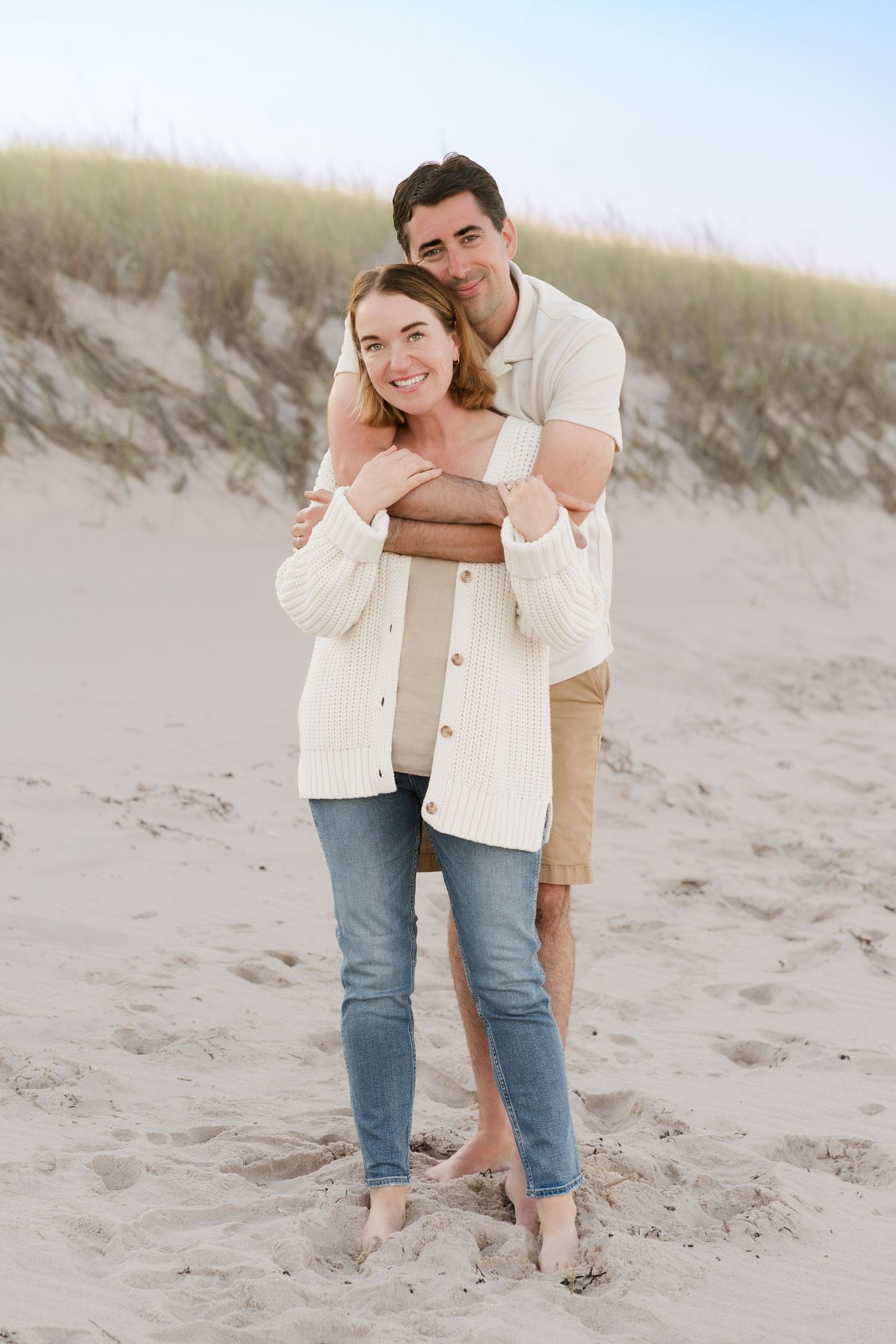 Couple embracing on sandy beach dunes during golden hour.