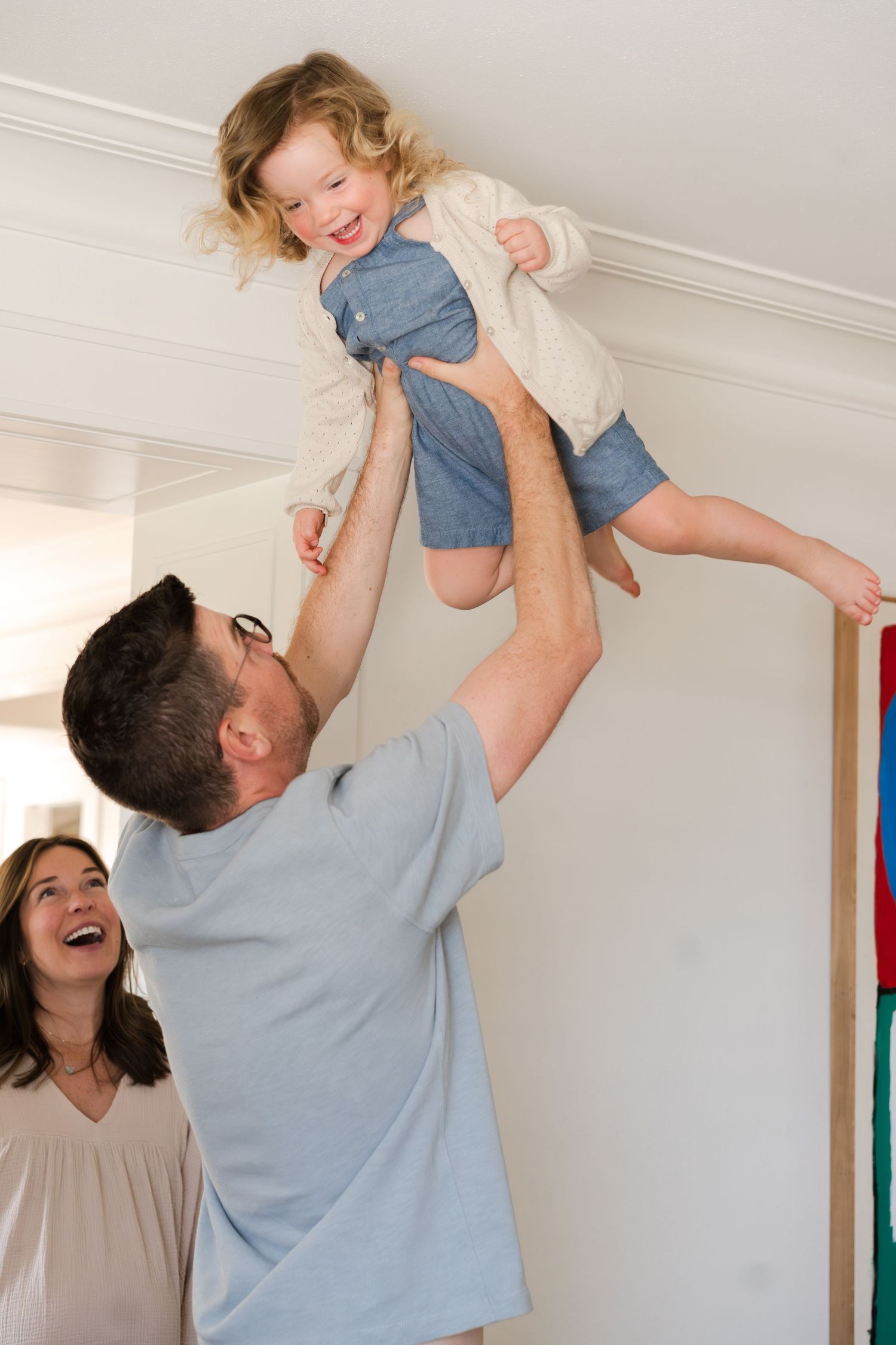 A joyful family moment with a child being lifted in the air while others laugh.