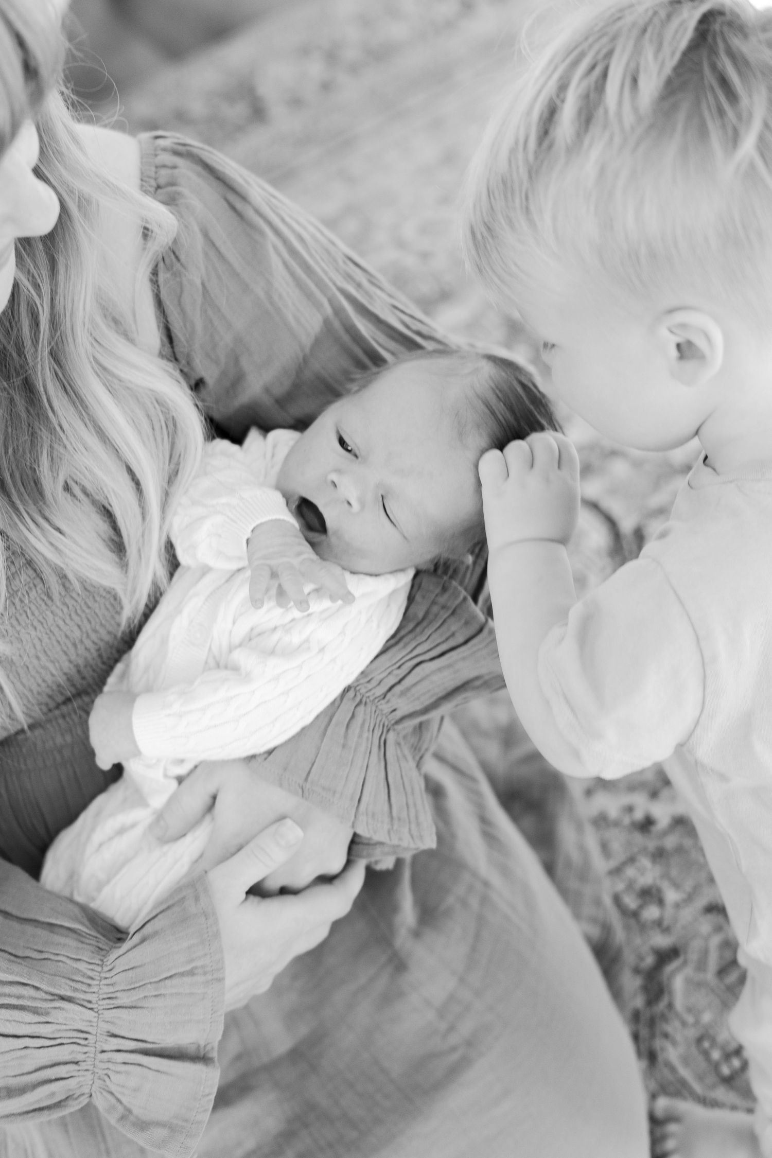Black and white photo of a sleeping newborn being tenderly watched by family members.