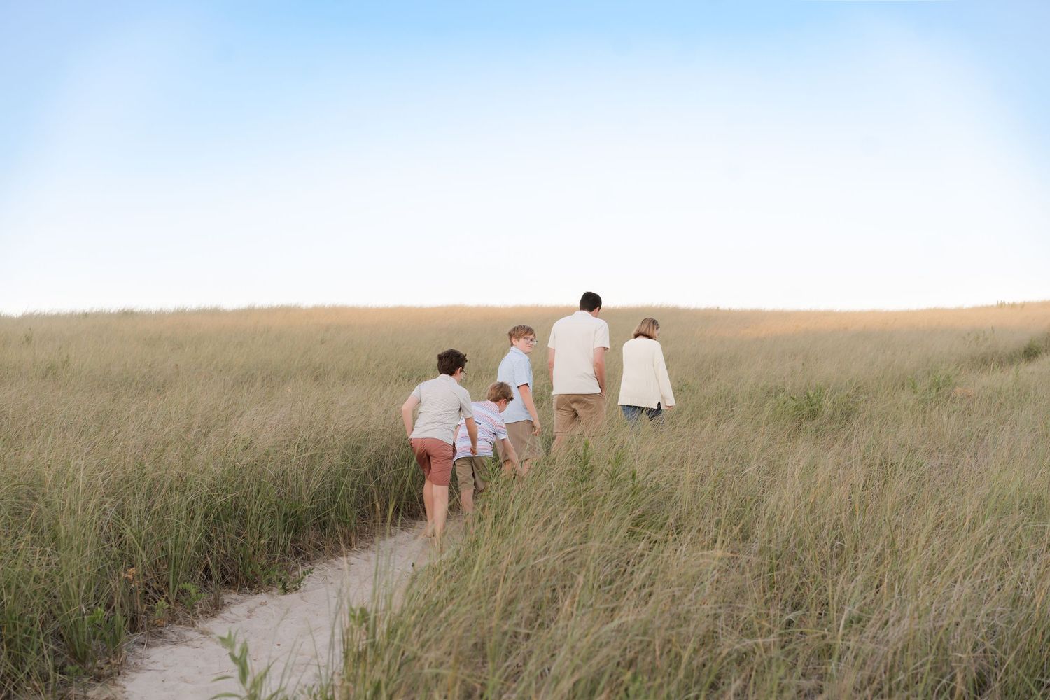 Family silhouetted against the sky while walking through seaside grassland.