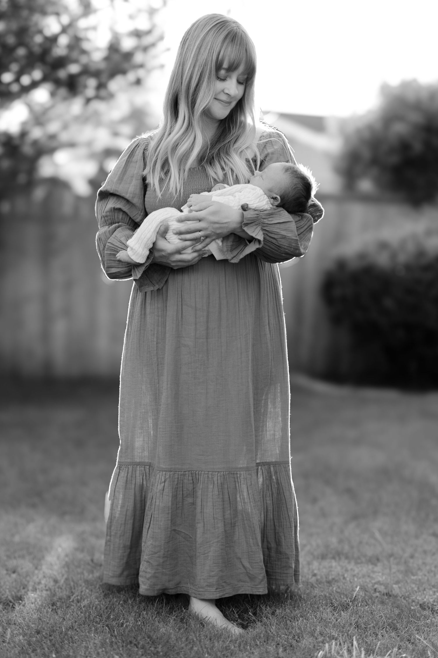 Black and white outdoor portraits of a woman in a flowing dress holding a baby.