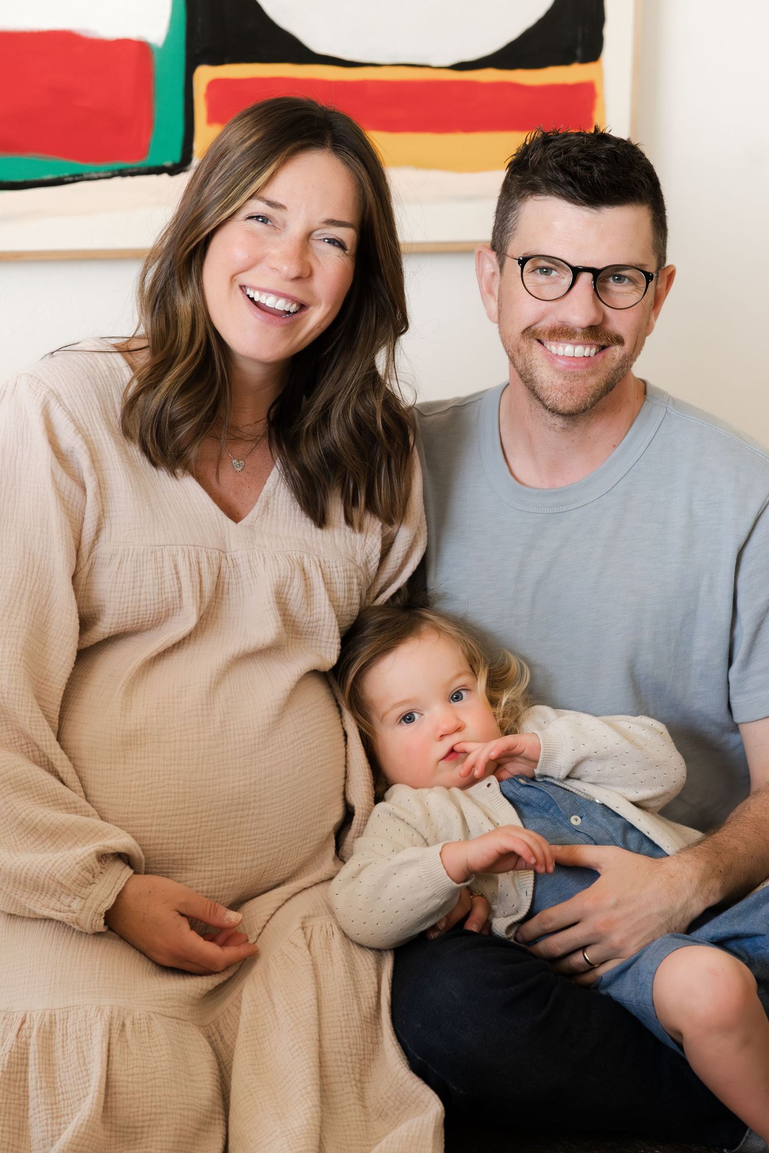 Family portrait with colorful abstract artwork hanging on the wall behind them.