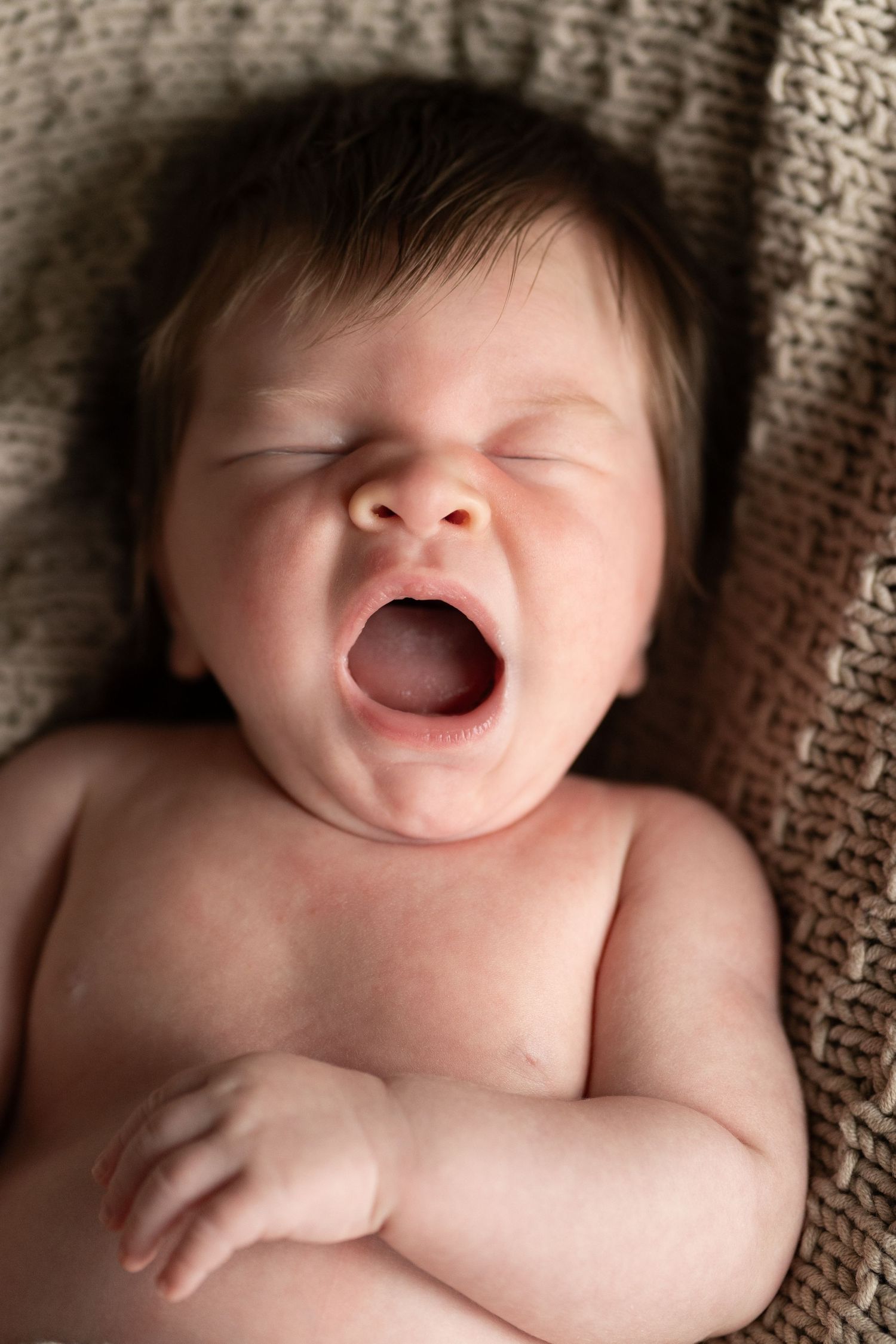 Baby expressing joy with wide smile while lying on knitted blanket.