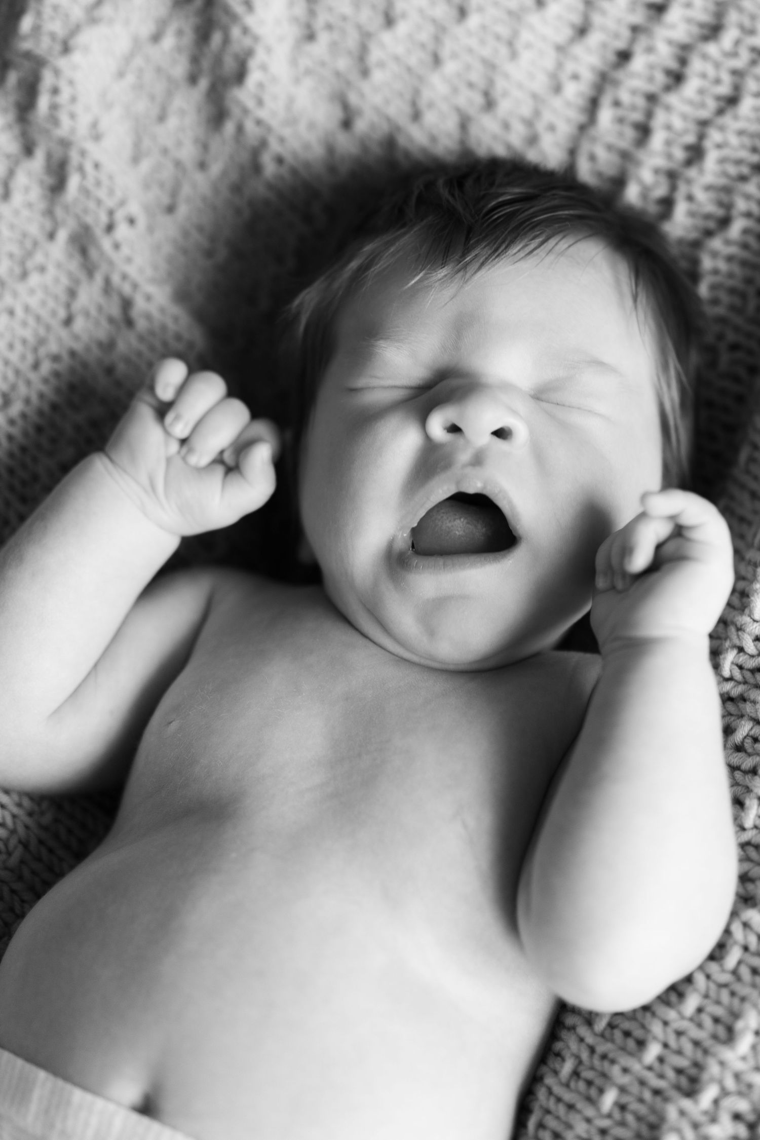 Black and white portrait of a sleeping baby on a textured blanket.