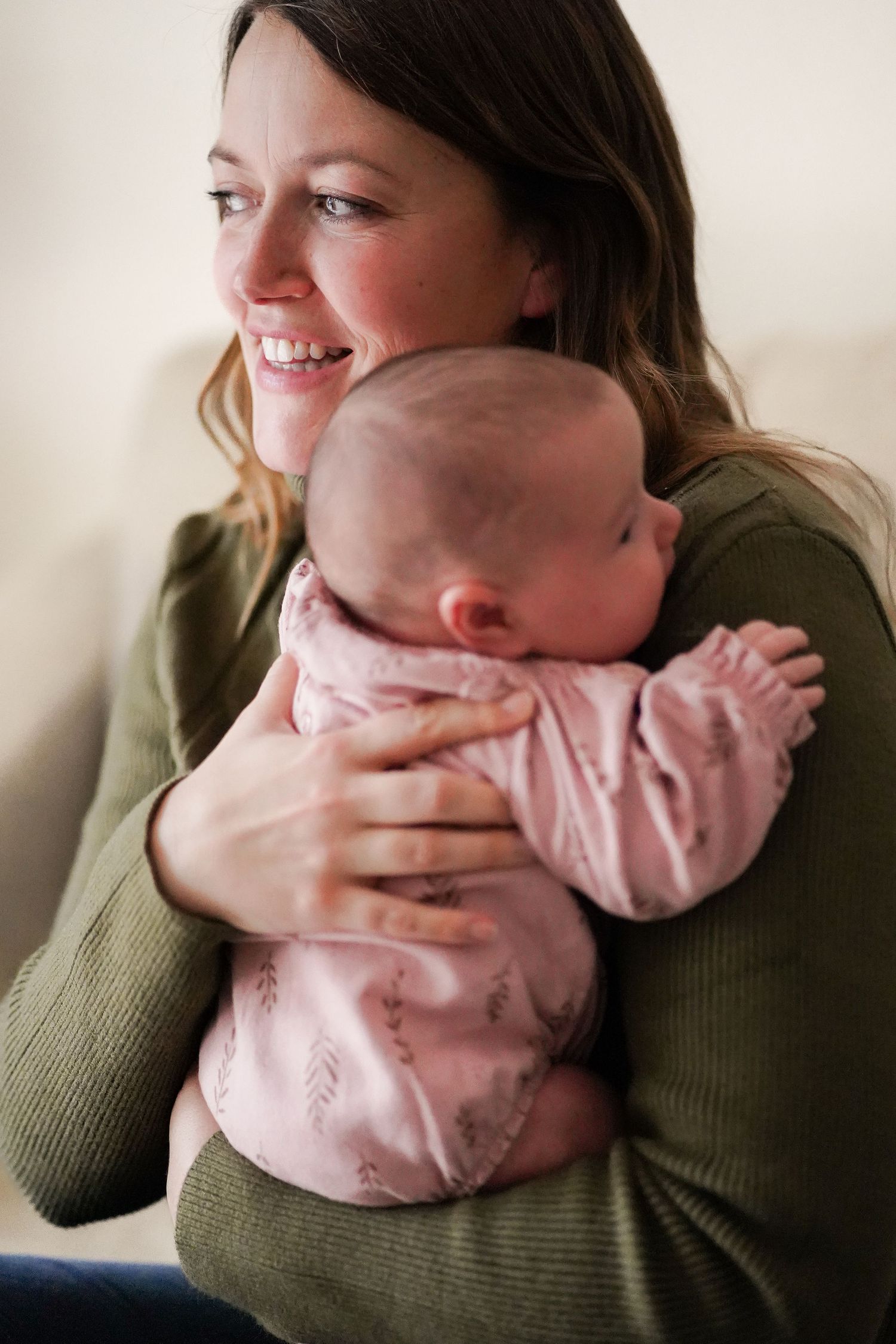 Woman in green sweater holding baby in pink outfit while smiling.