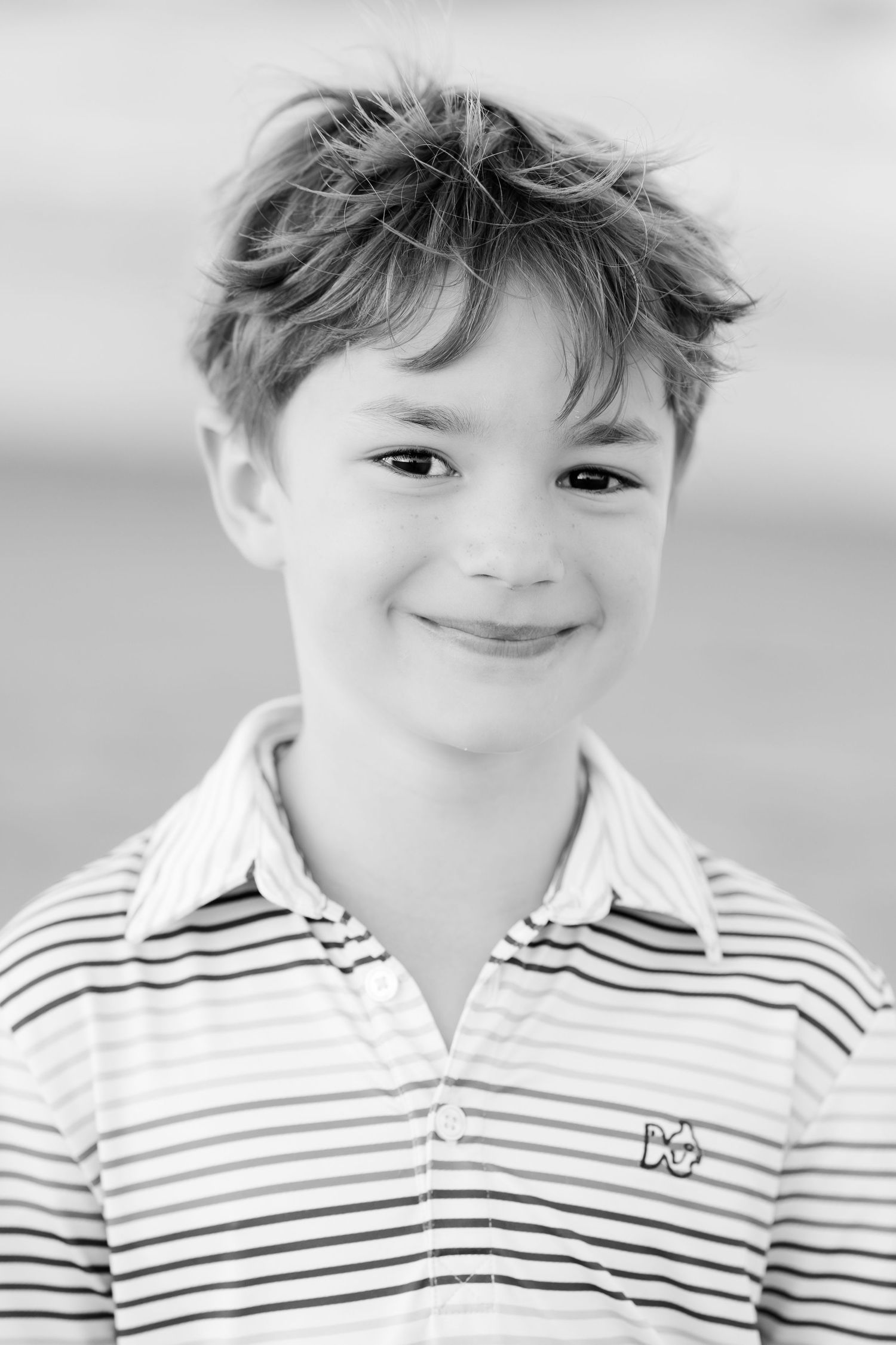 Black and white close-up portrait of a young person in a striped polo shirt.