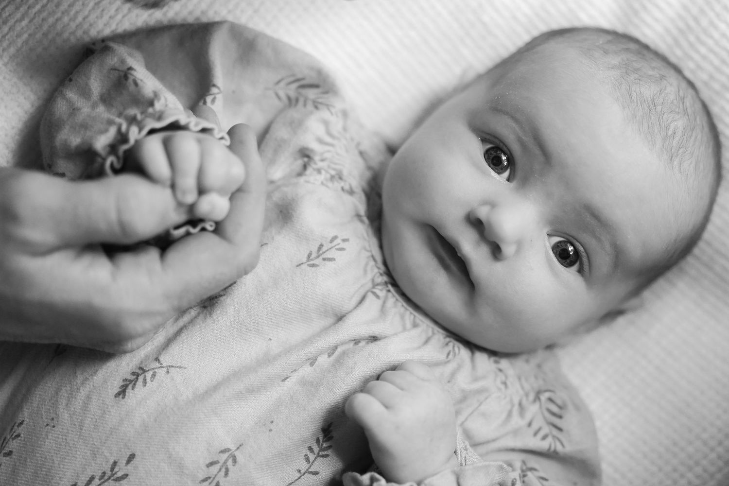 Black and white portrait of baby in patterned outfit with hands visible.